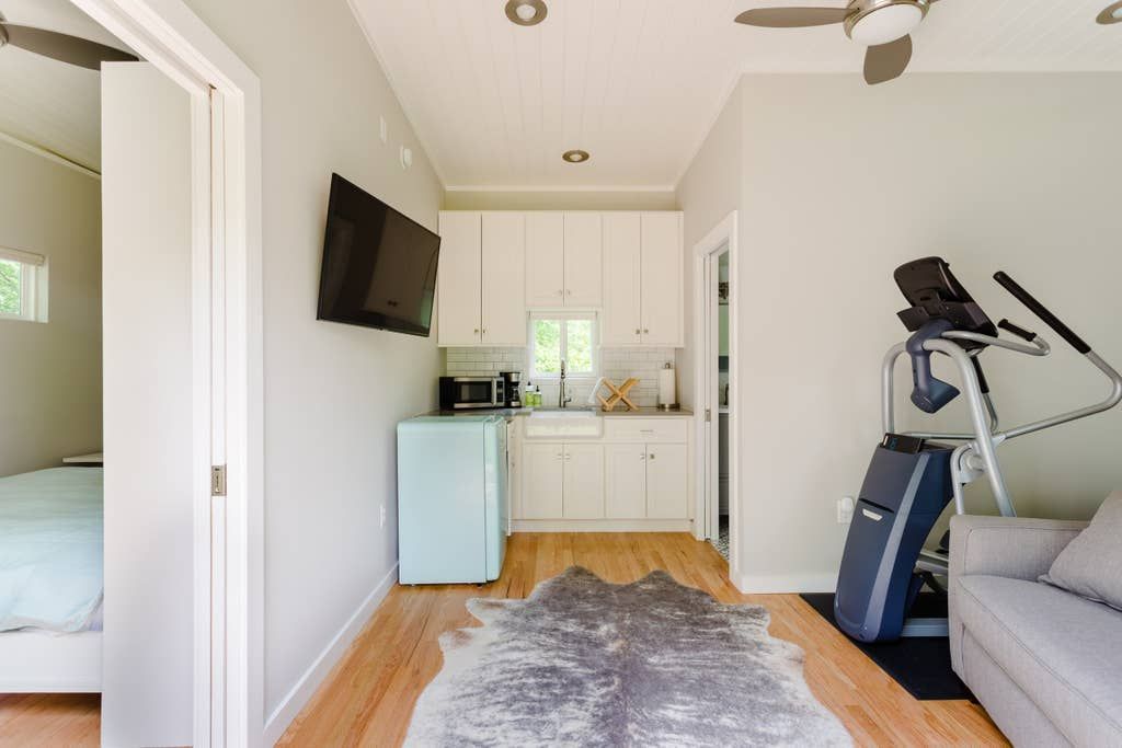 Small room with kitchenette, treadmill, sofa, cowhide rug, and TV.