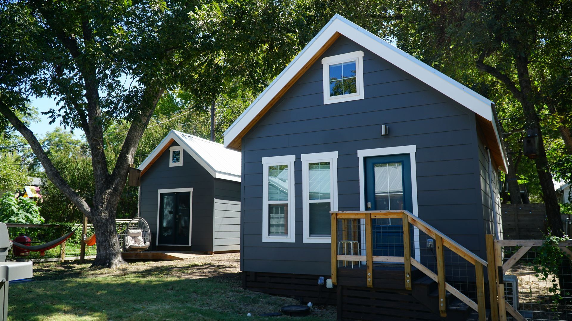 Two small blue houses with white trim, a yard, and trees.