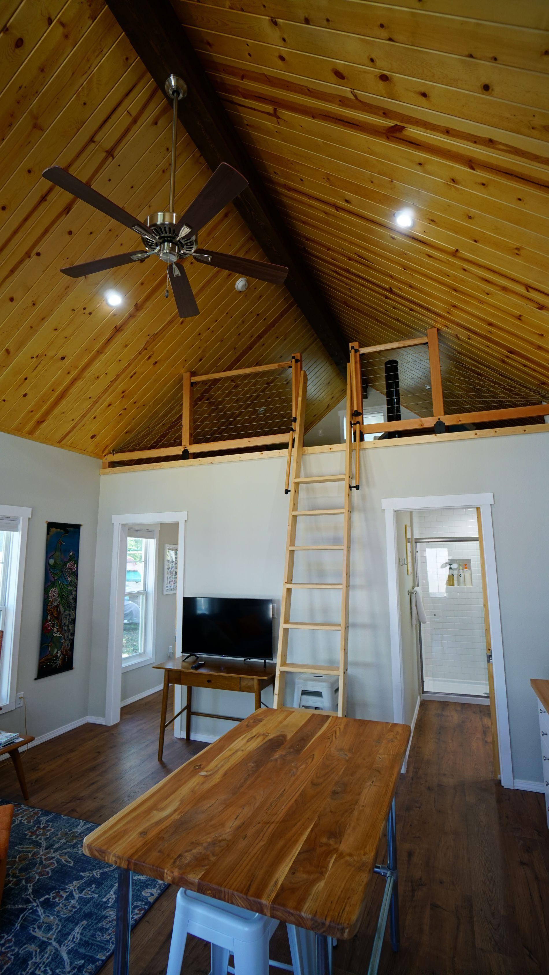 Cozy interior with loft. Wooden ceiling, ladder, island, tv, and open doorways.