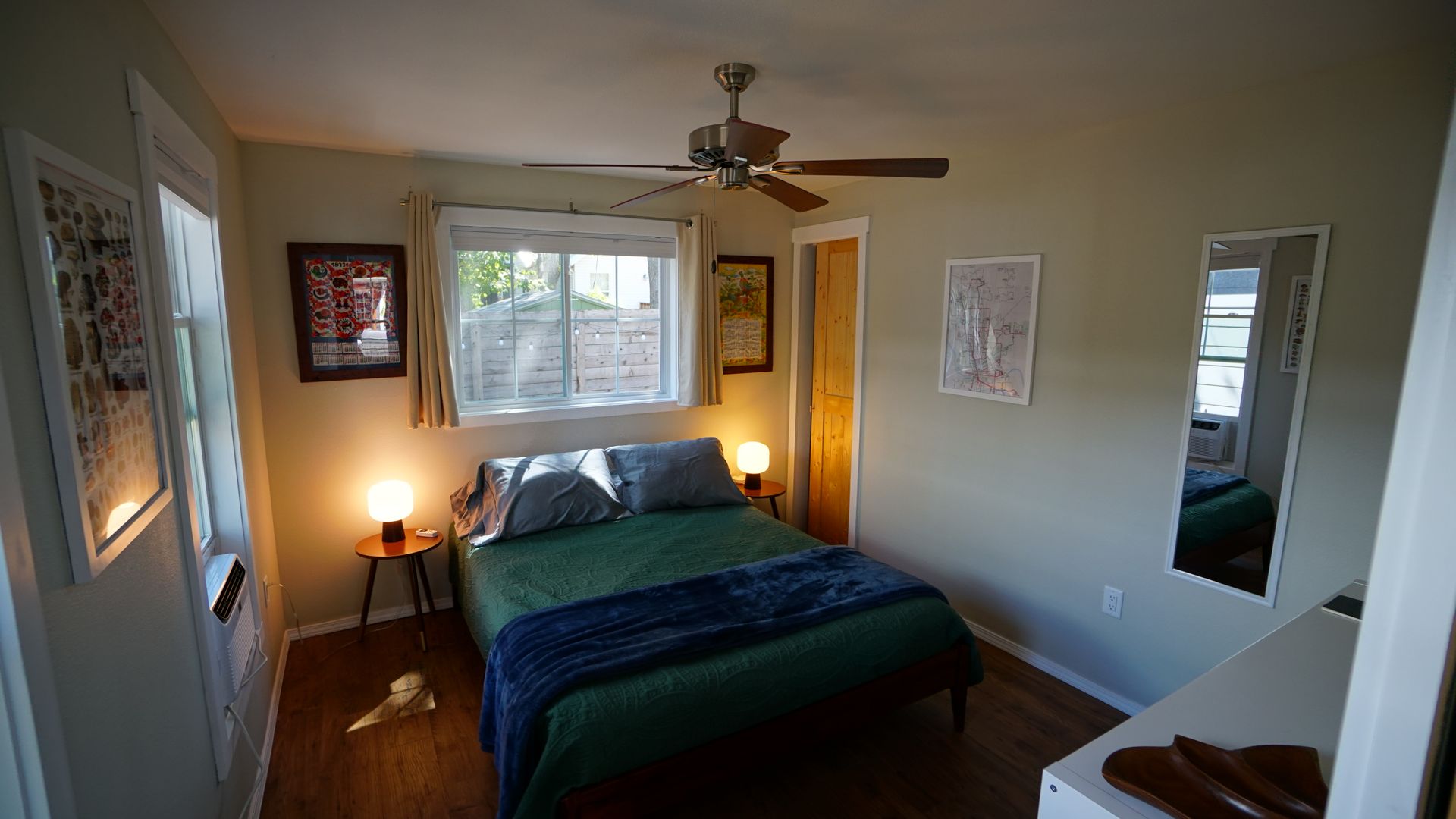 Small bedroom with a bed, two windows, art, mirror, and two bedside lamps.