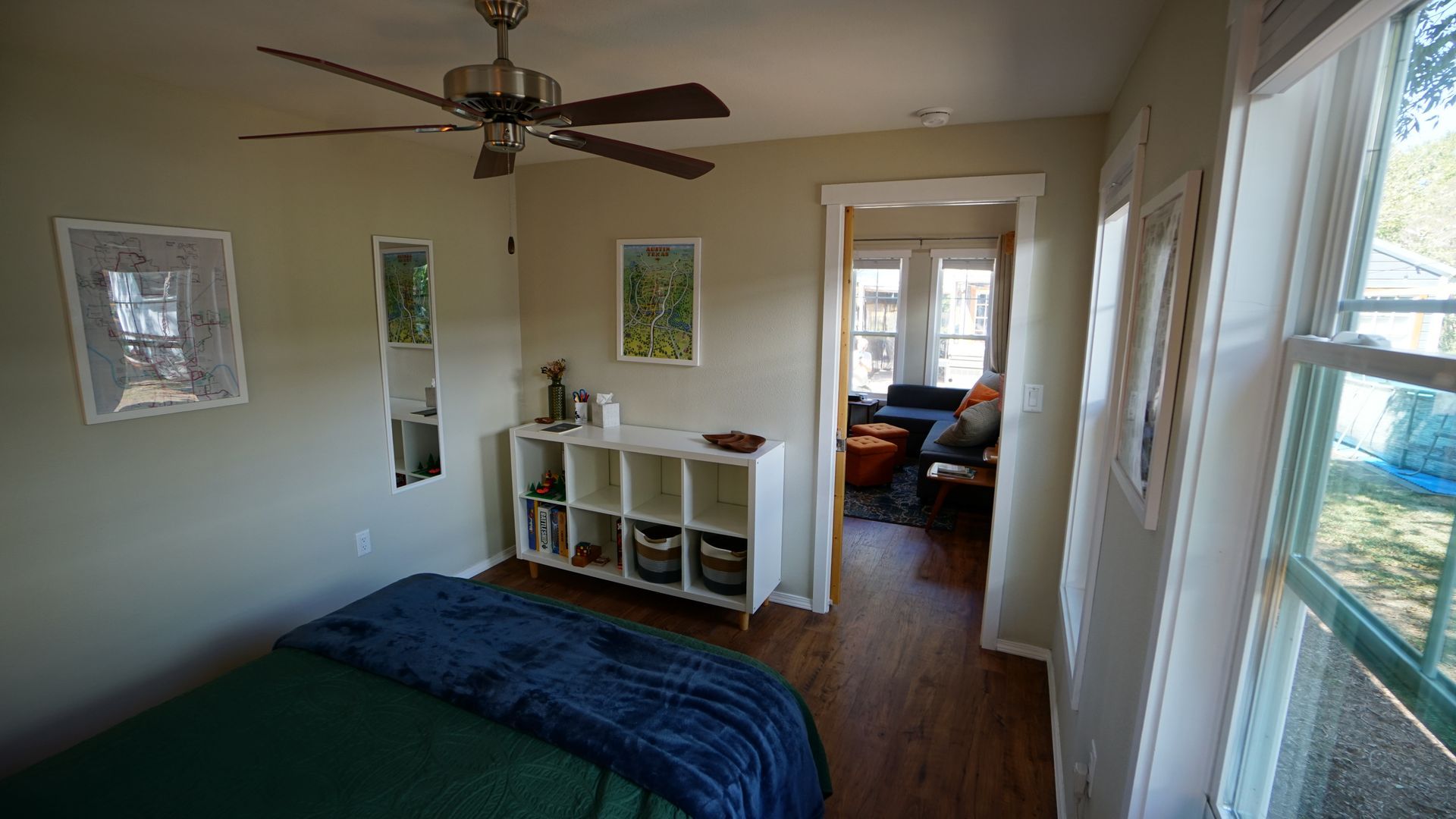 Bedroom with bed, storage, and doorway to another room. Green walls, wood floors, and ceiling fan.