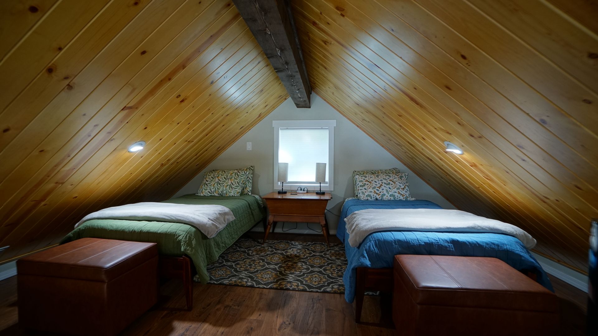 Two twin beds in a wood-paneled attic bedroom, with storage ottomans and a small window.