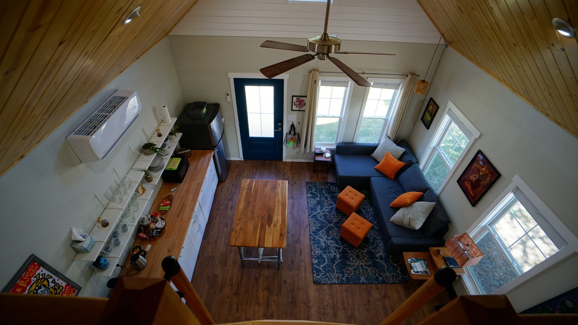 Overhead view of a living space: wood ceiling, blue sectional, coffee table, windows, and open doorway.