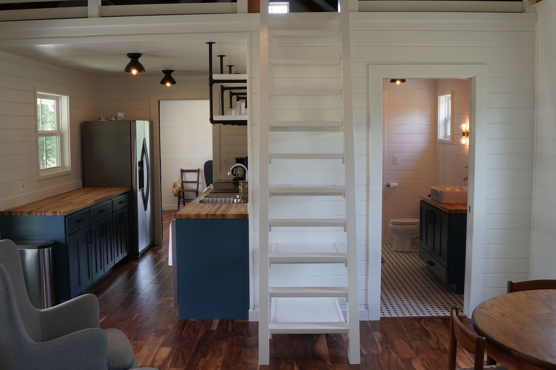 Interior view of a tiny house with a ladder, kitchen, and bathroom.