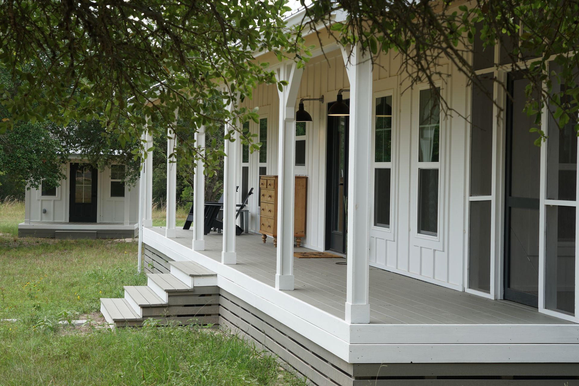 White farmhouse with a wraparound porch, steps, and a separate structure in a grassy field.