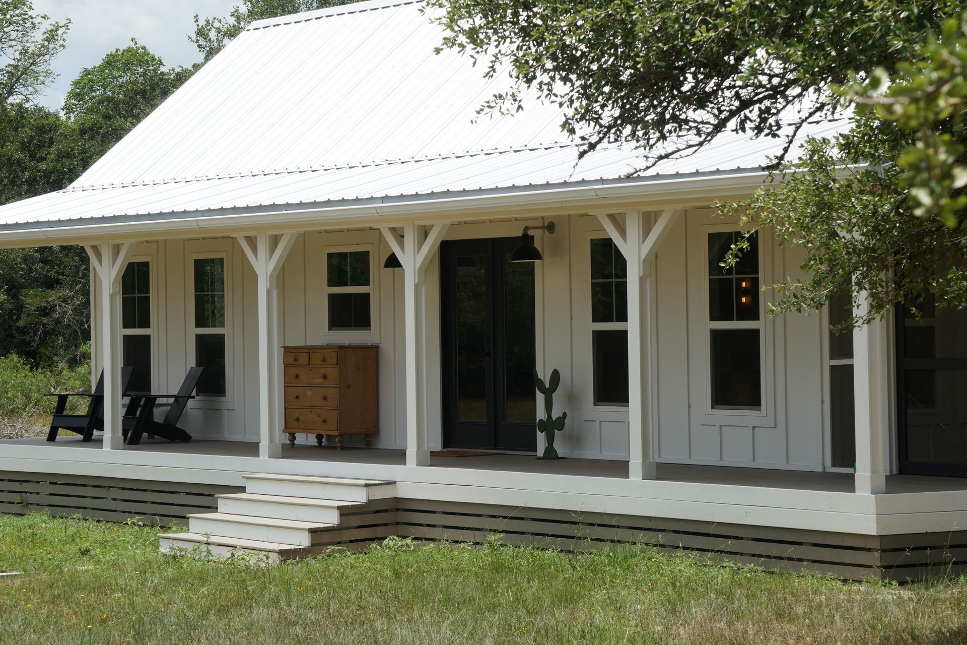 White farmhouse with porch and metal roof in a grassy field.
