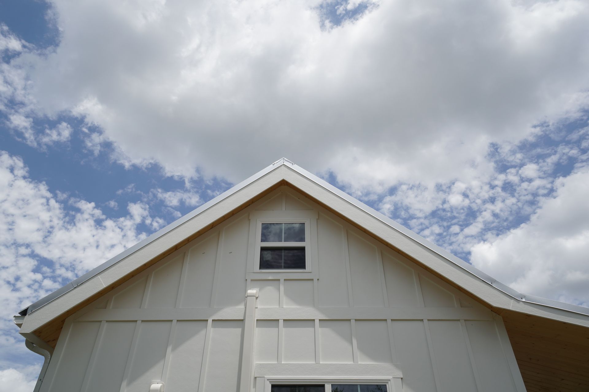 White gabled house with a metal roof and a small window against a blue sky with fluffy clouds.