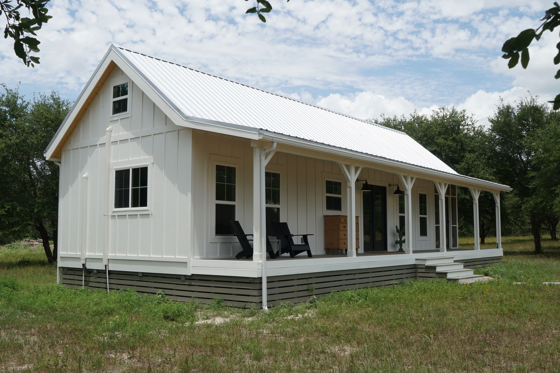 White farmhouse with a porch and metal roof in a grassy field.
