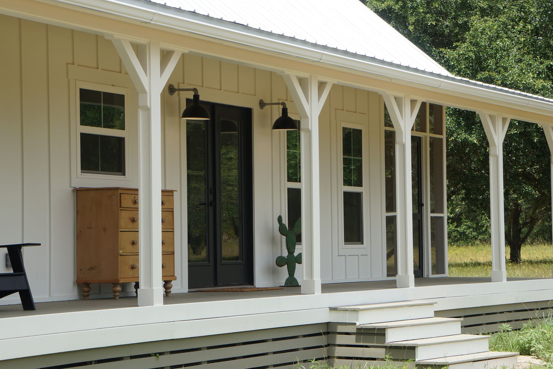 White farmhouse with porch, black doors, and black sconces.