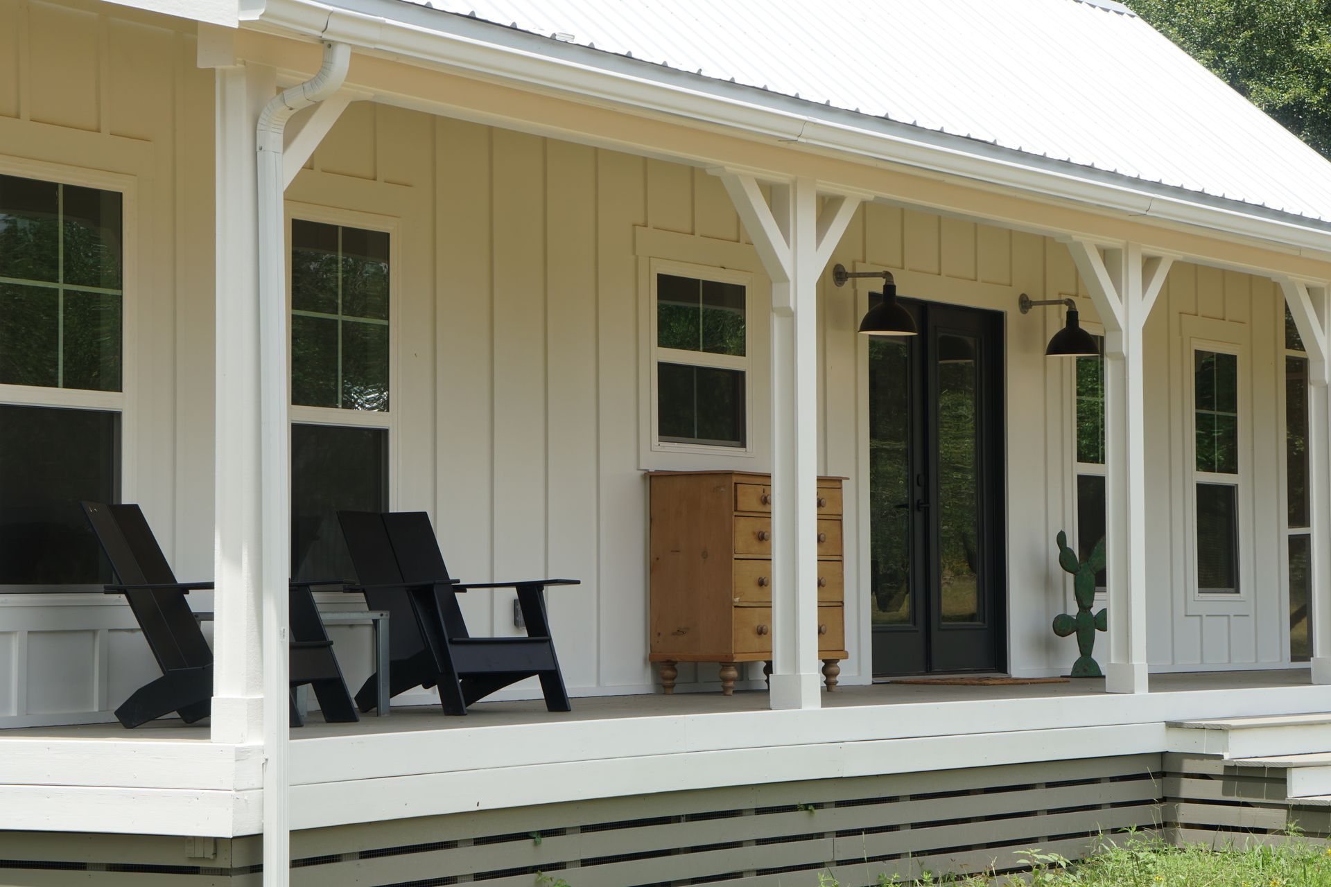 White farmhouse porch with black chairs and doors, with a wooden cabinet and cactus.