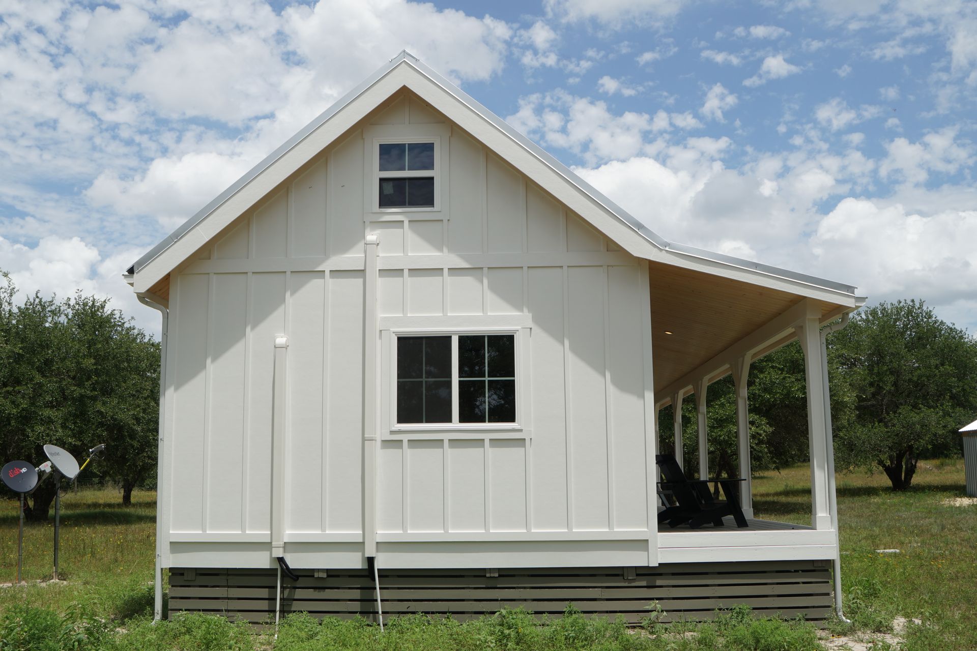 White farmhouse with porch and metal roof on a sunny day.