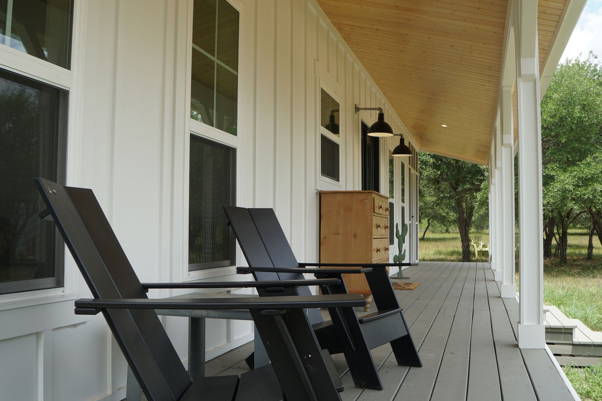 Two black chairs on a white porch of a house with a wooden ceiling.