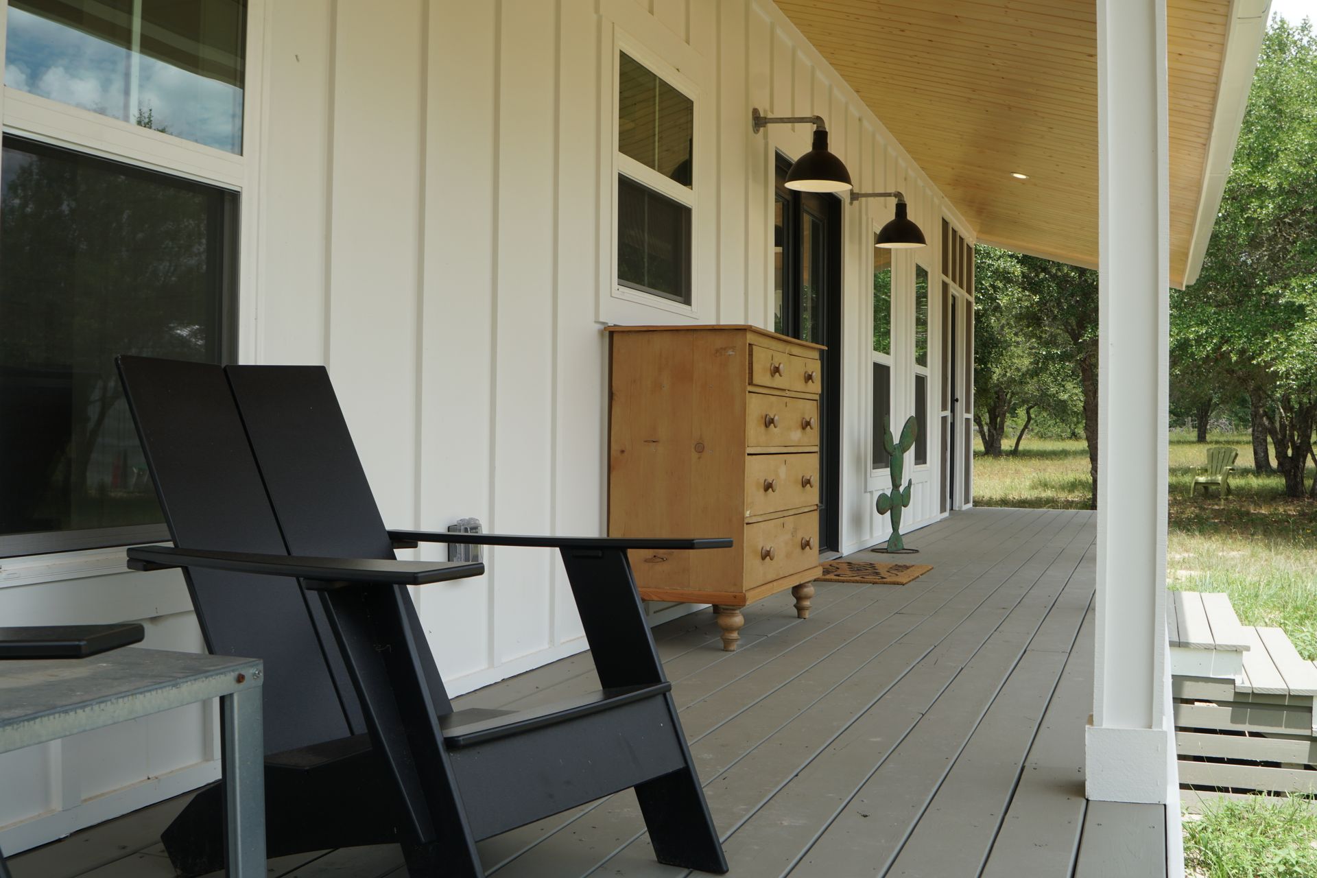 A black modern chair on a white porch with a wooden chest and wall-mounted lights.