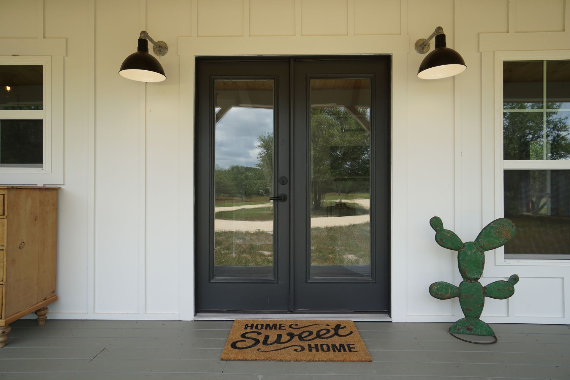 Black double doors with glass panels, flanked by windows and black barn-style lights on a white exterior.