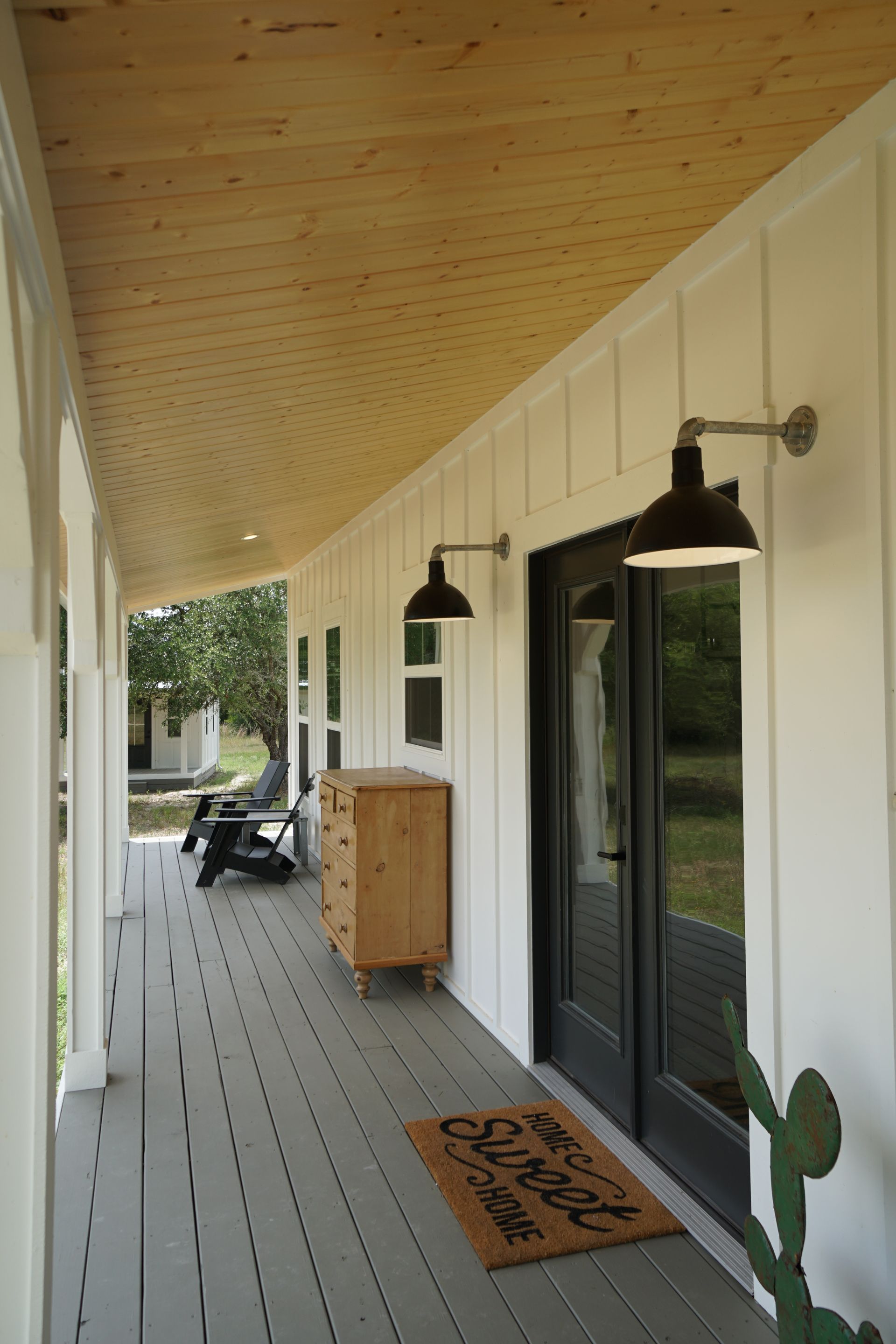 Covered porch with white siding, gray floorboards, black doors, and black sconces.