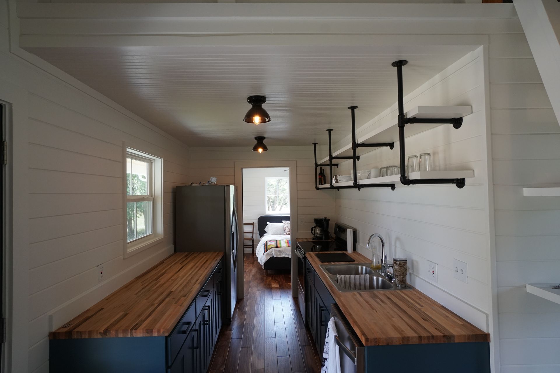 Narrow, modern kitchen with wooden countertops, black cabinets, and open shelving.