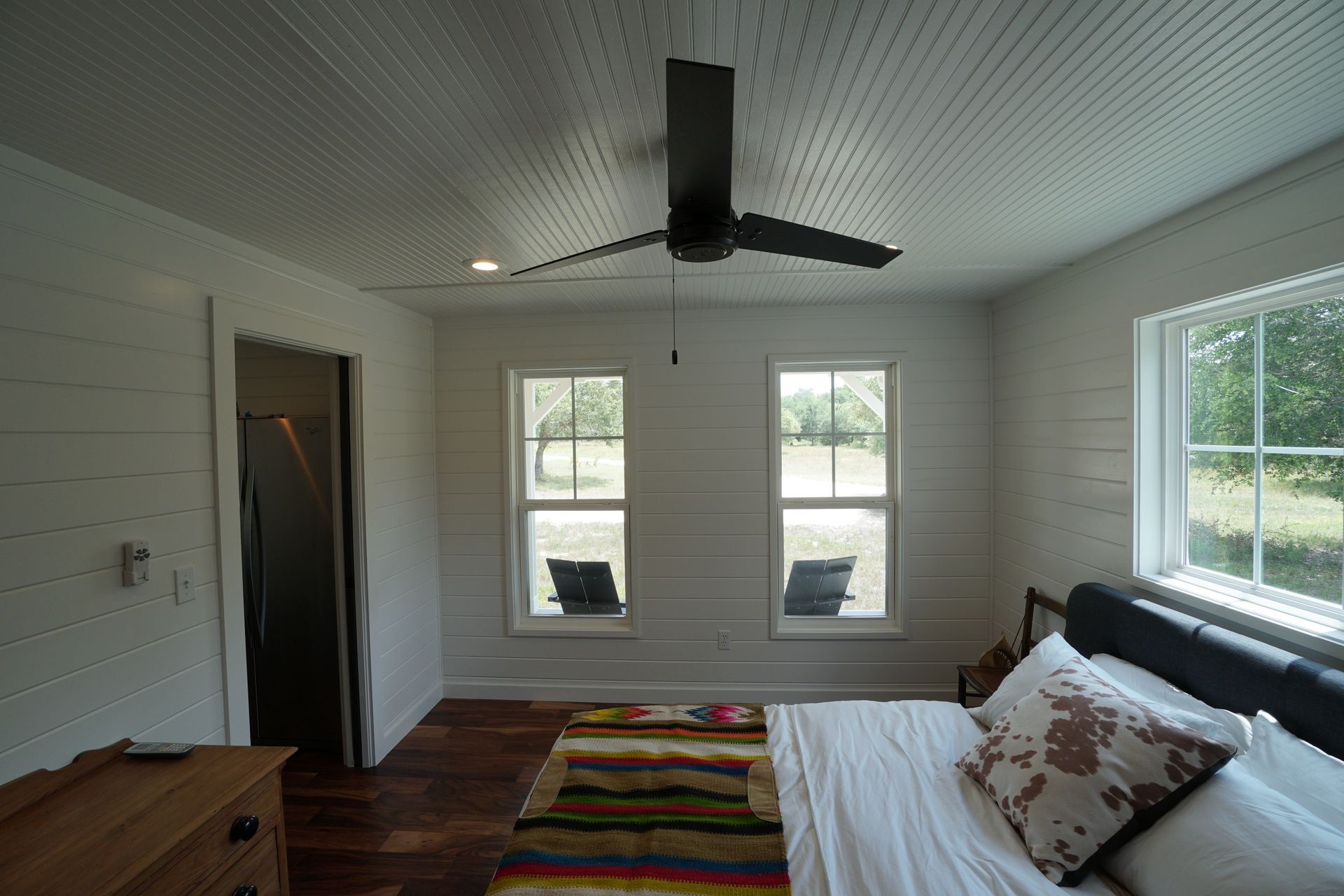 White bedroom with a ceiling fan, two windows, and a bed.