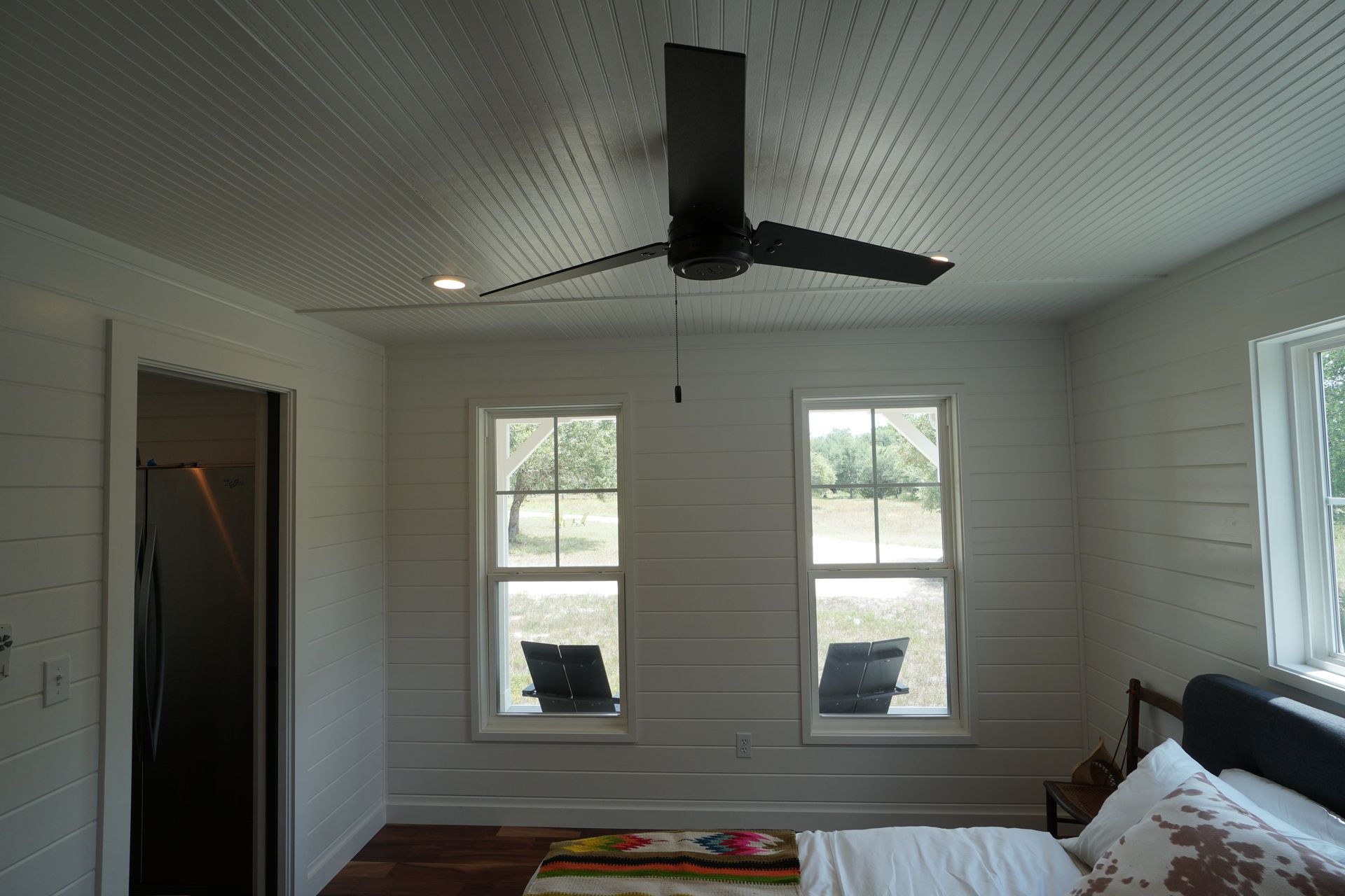 Bedroom with a dark ceiling fan, two windows, white plank walls, and a bed.