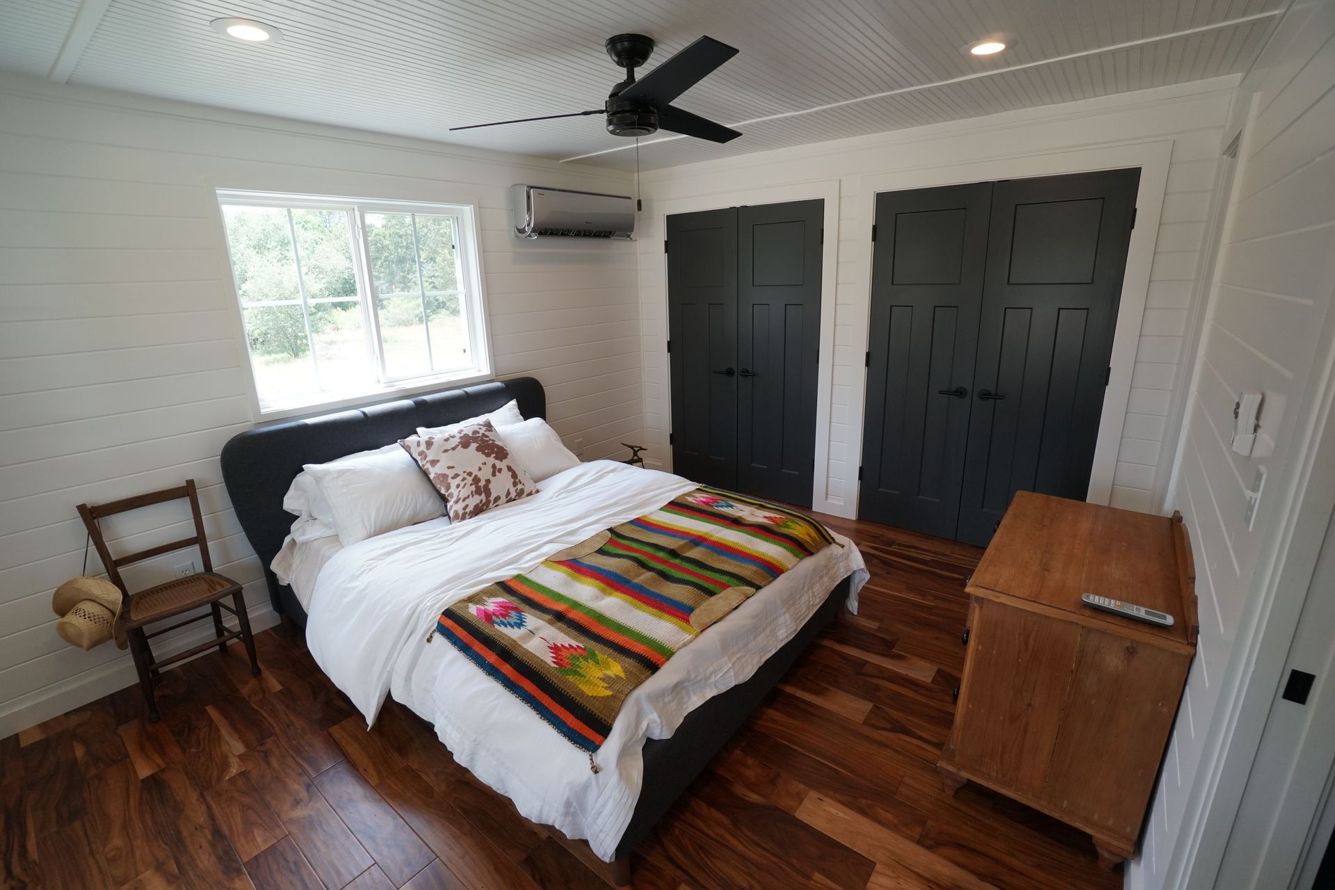 Bedroom with a bed, two dark closets, a wooden dresser, and a ceiling fan.