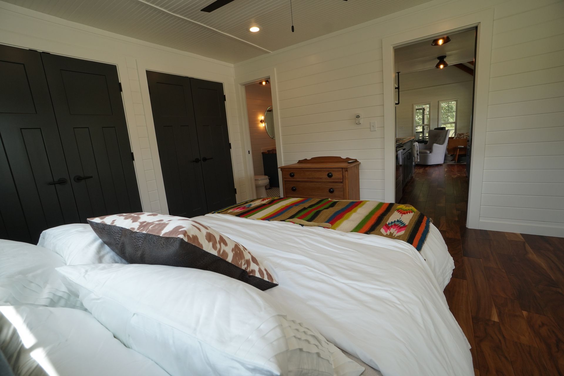 Bedroom with white bedding, brown pillow, two black closets, and wood floors.