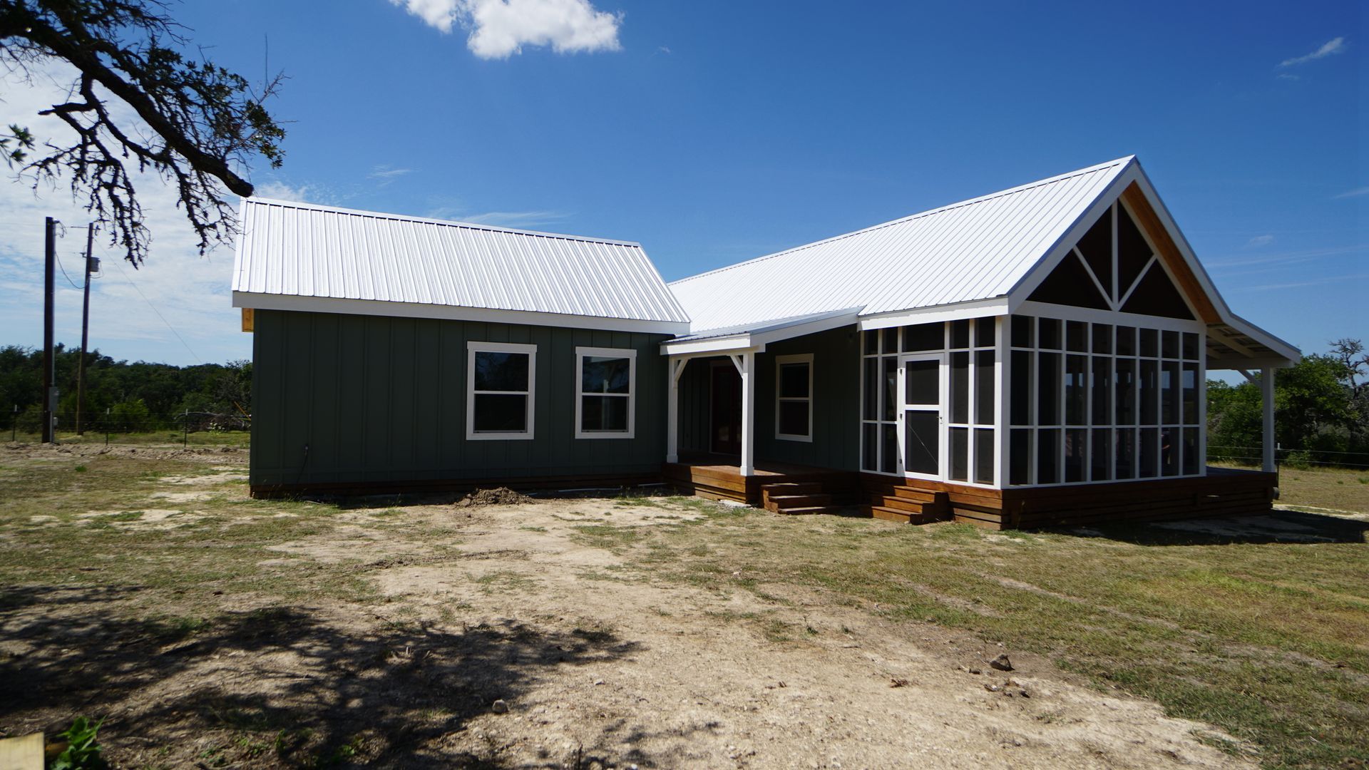 Green house with white roof, porch with screen, in a field under a bright blue sky.