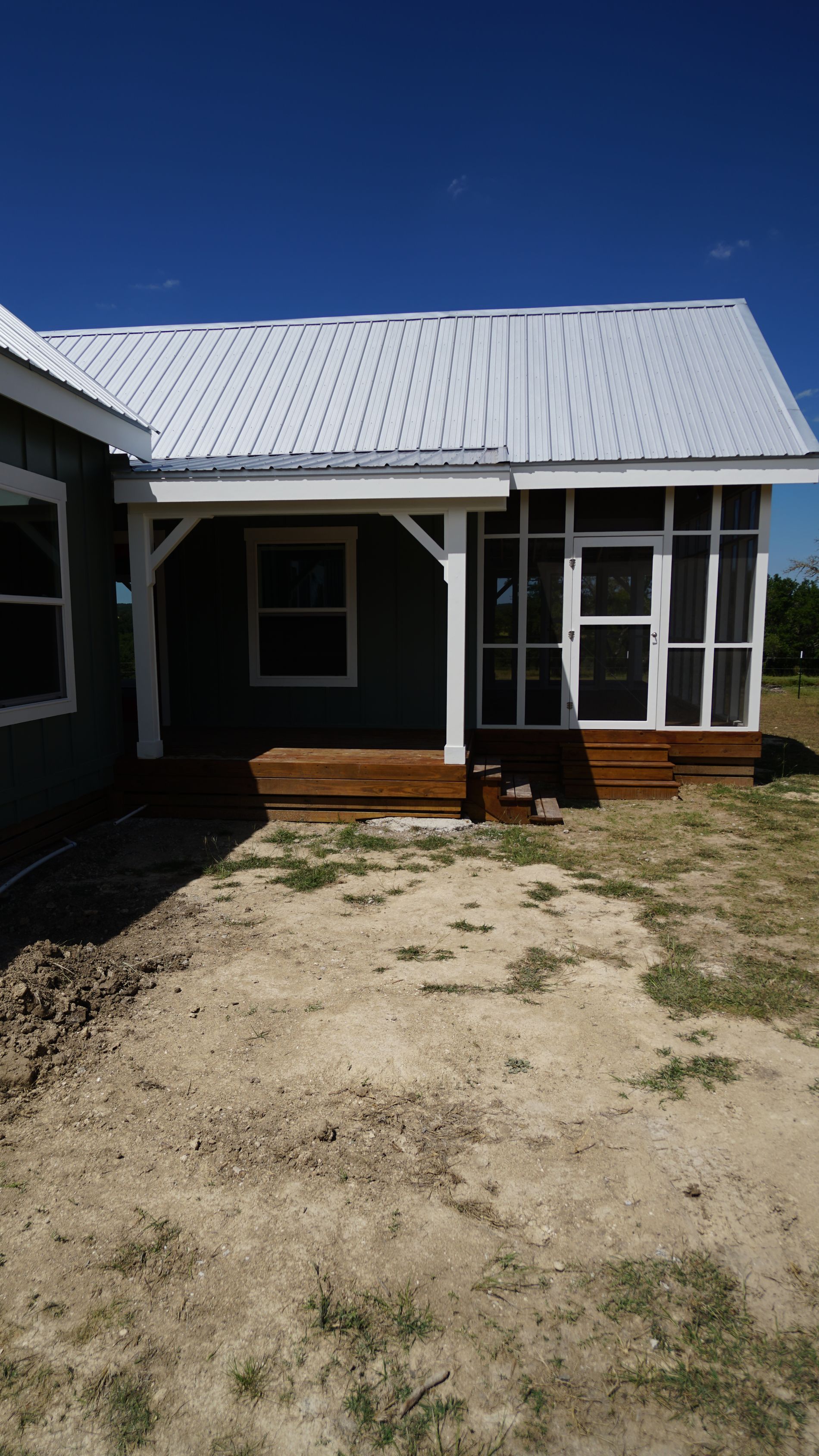 Blue house with white trim, porch, and screened-in area; bright white metal roof; sunny, dirt yard.