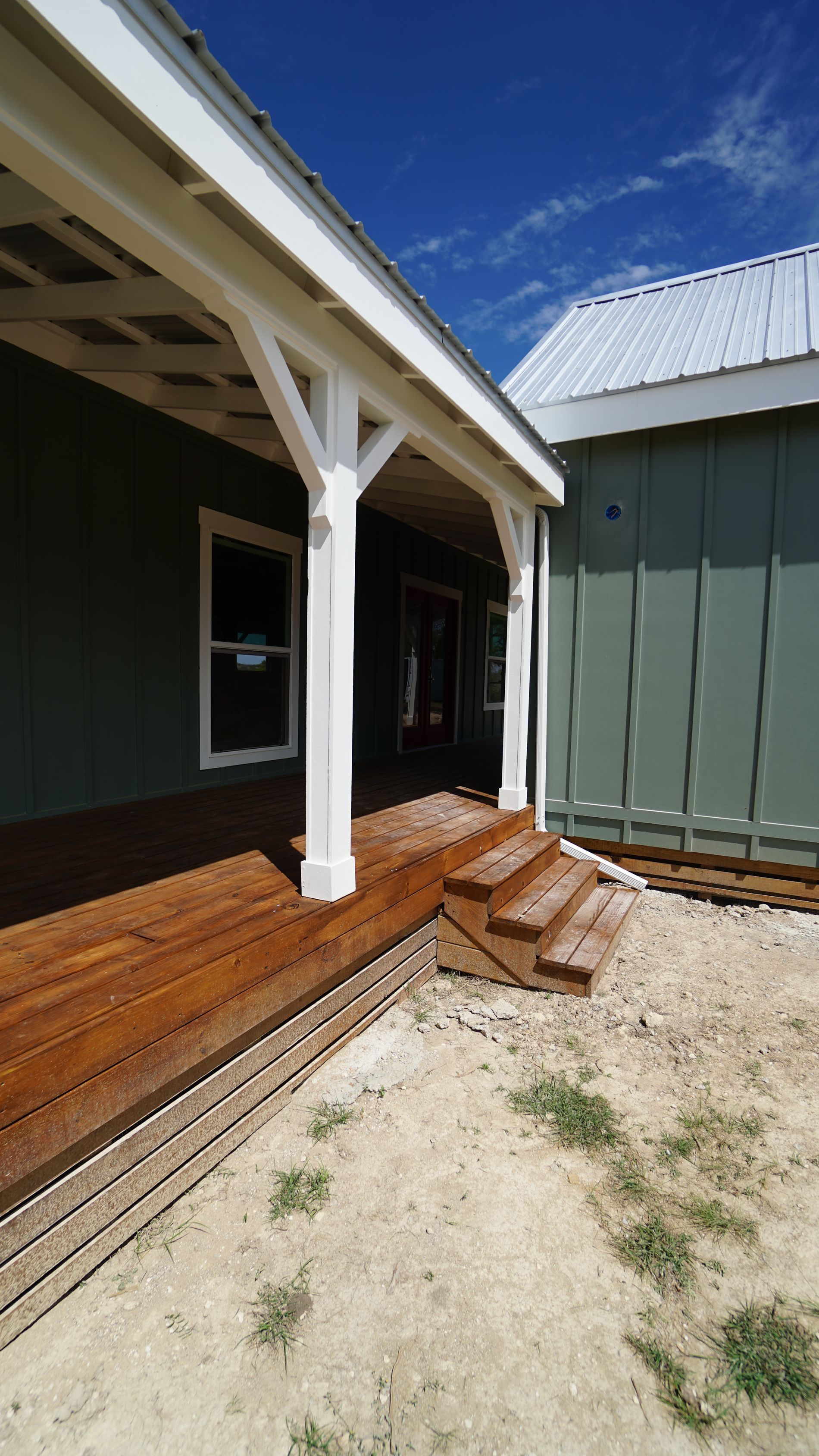 Wooden porch with steps leading to a green building with white trim.