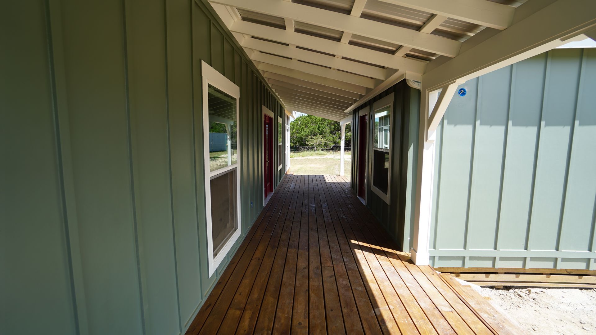 Covered porch with wood decking and teal siding. A white ceiling and windows are visible.