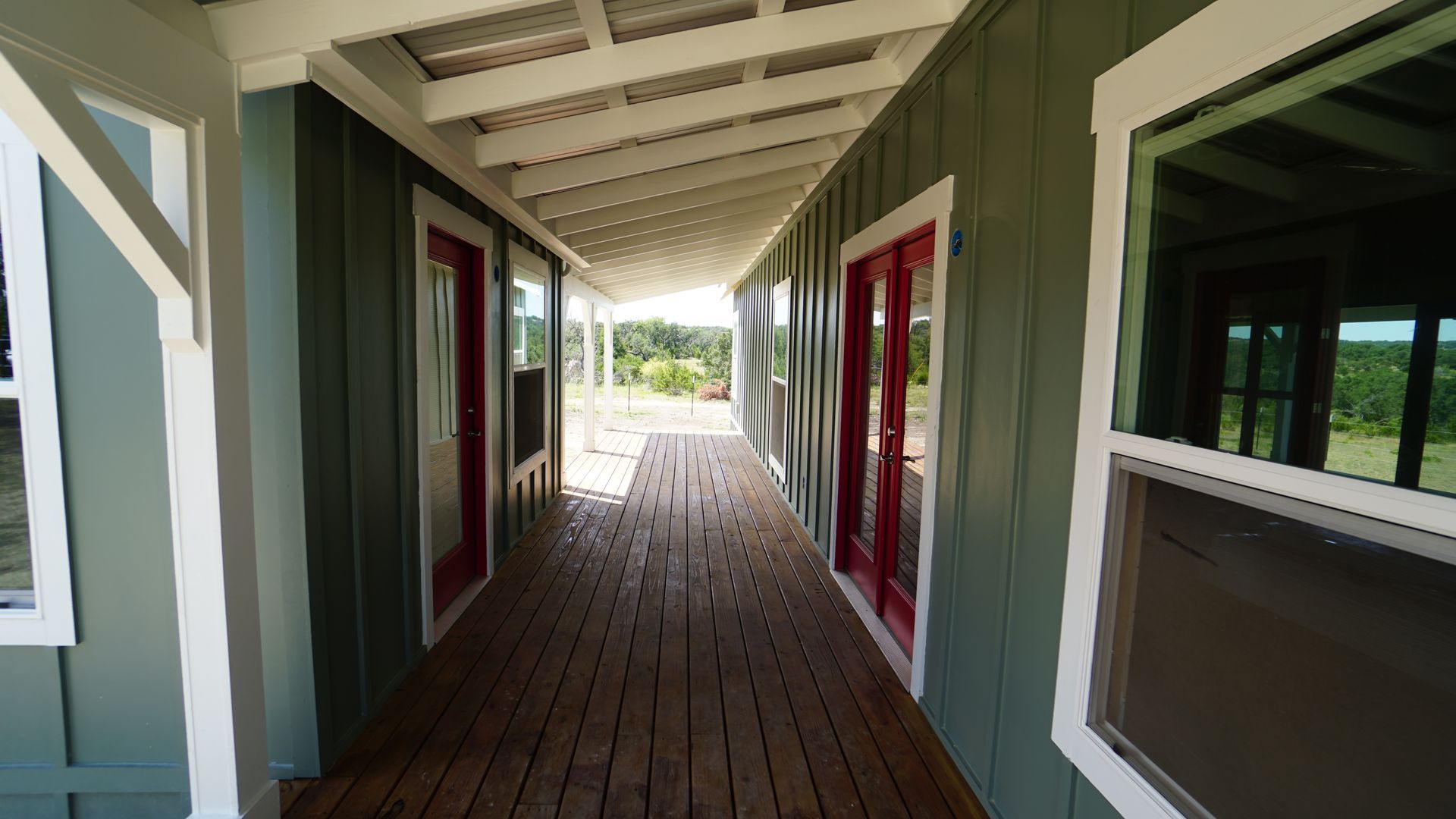 Covered porch with green siding, red doors, and wood decking. White trim and ceiling.