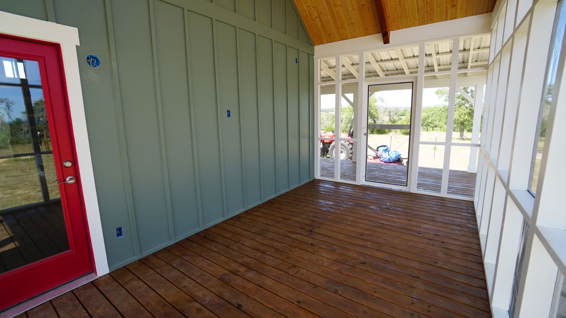 Covered porch with red door, wood floor, screen enclosure, and green siding.