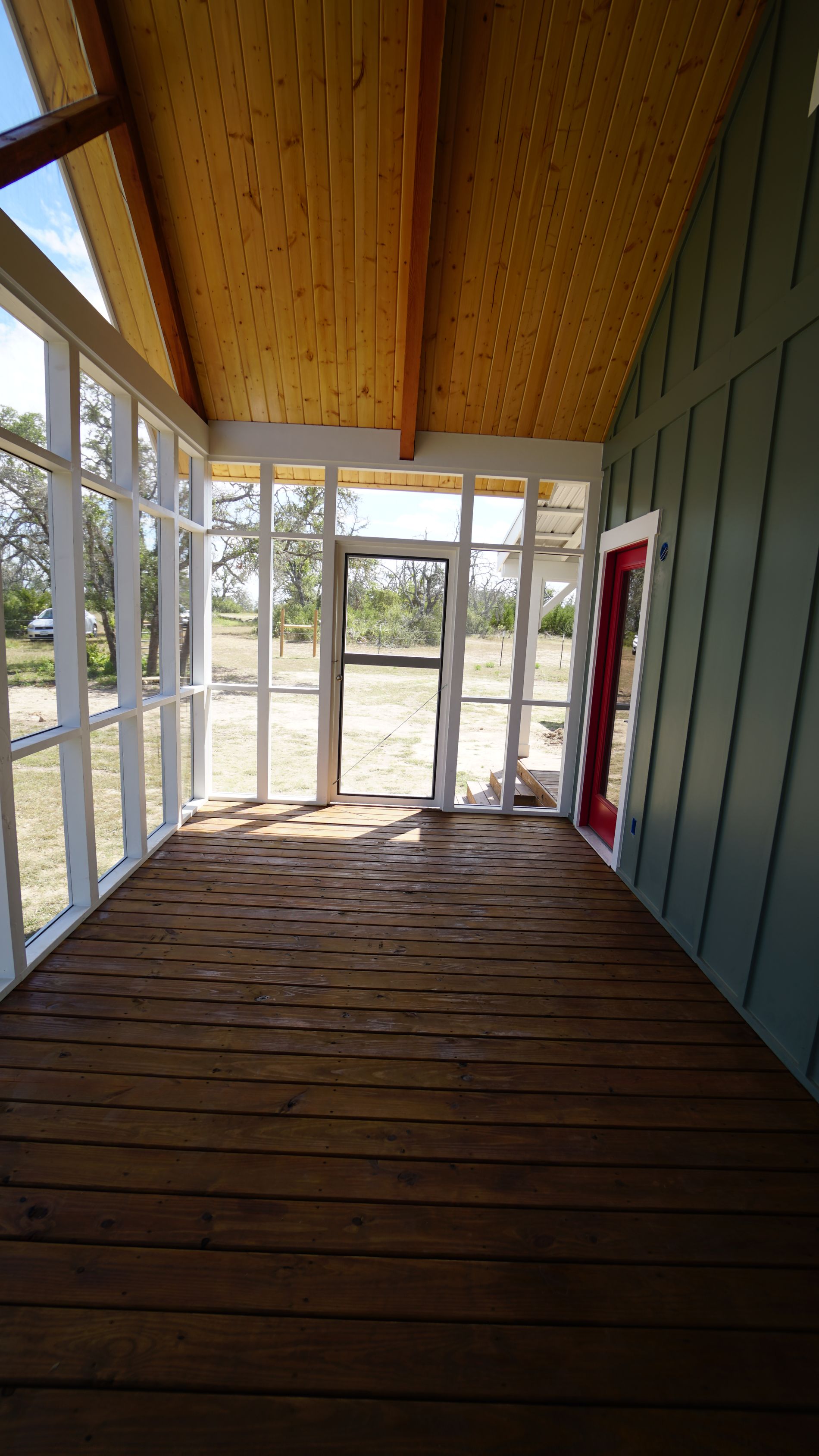 Sunroom with wooden floor, screens, and door. Green exterior wall with red trim.