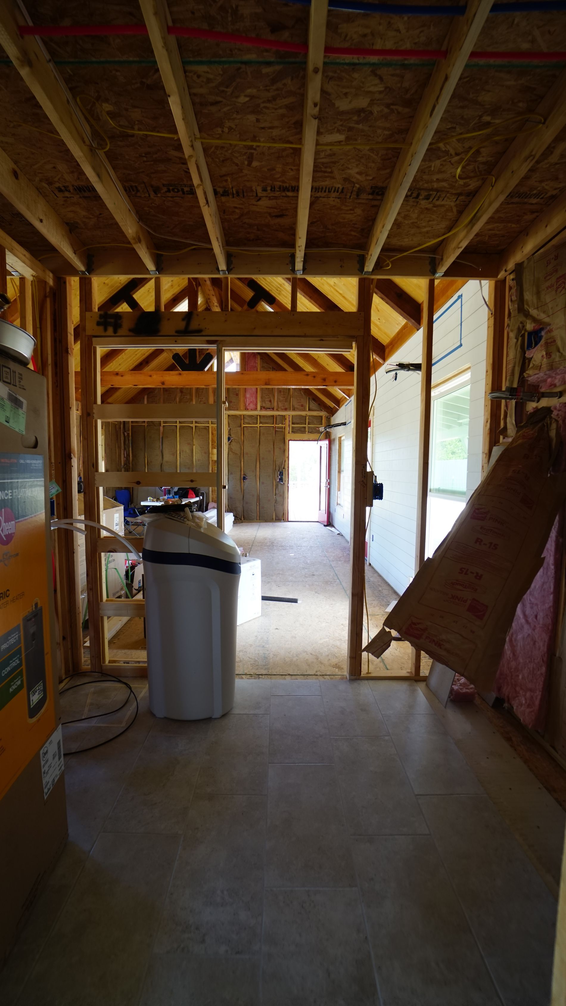Interior view of a building under construction, framed walls, open doorway, with a water softener visible.