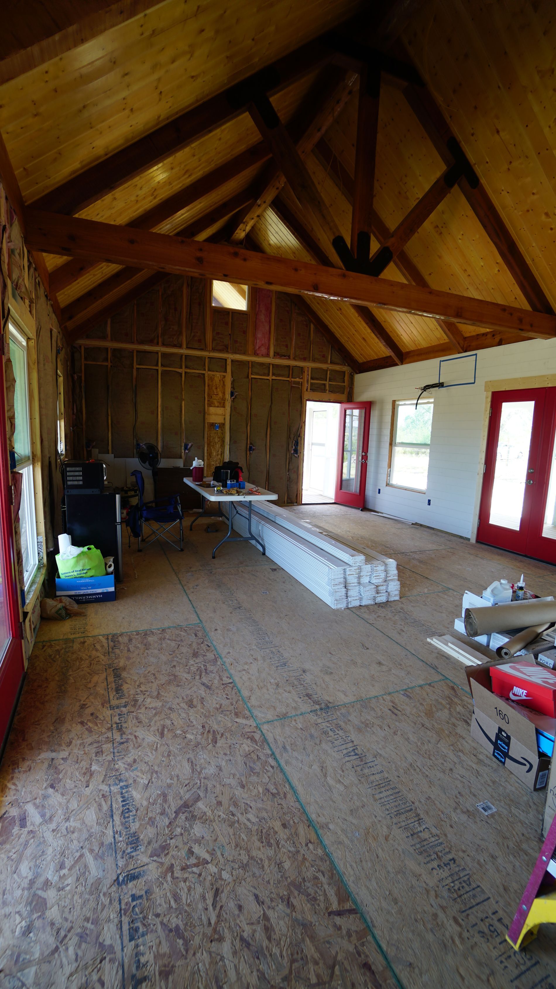 Interior of a house under construction; exposed wooden beams, unfinished walls, flooring, doors, and window frames.