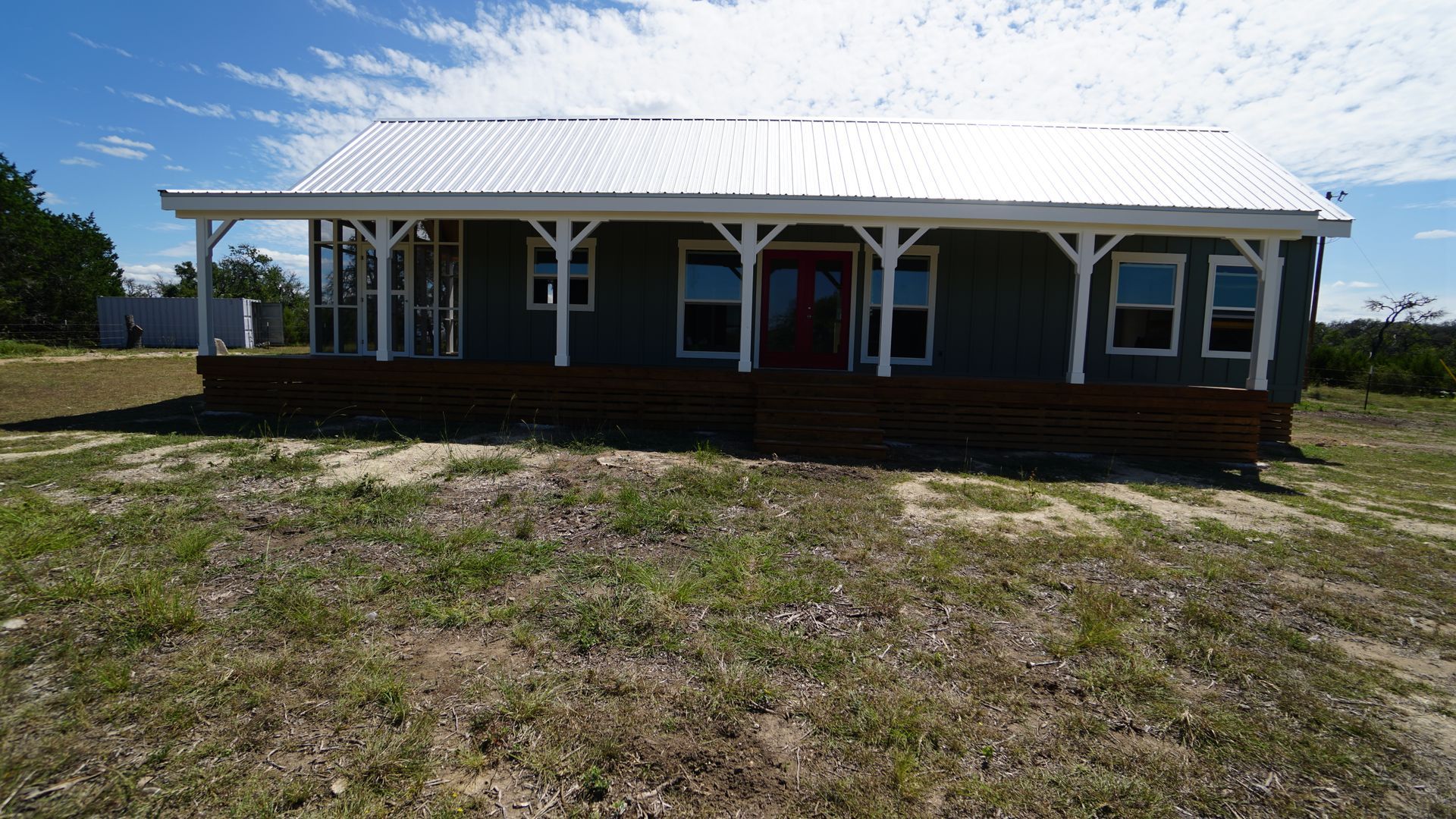 Green house with white porch and corrugated metal roof on a grassy plot.