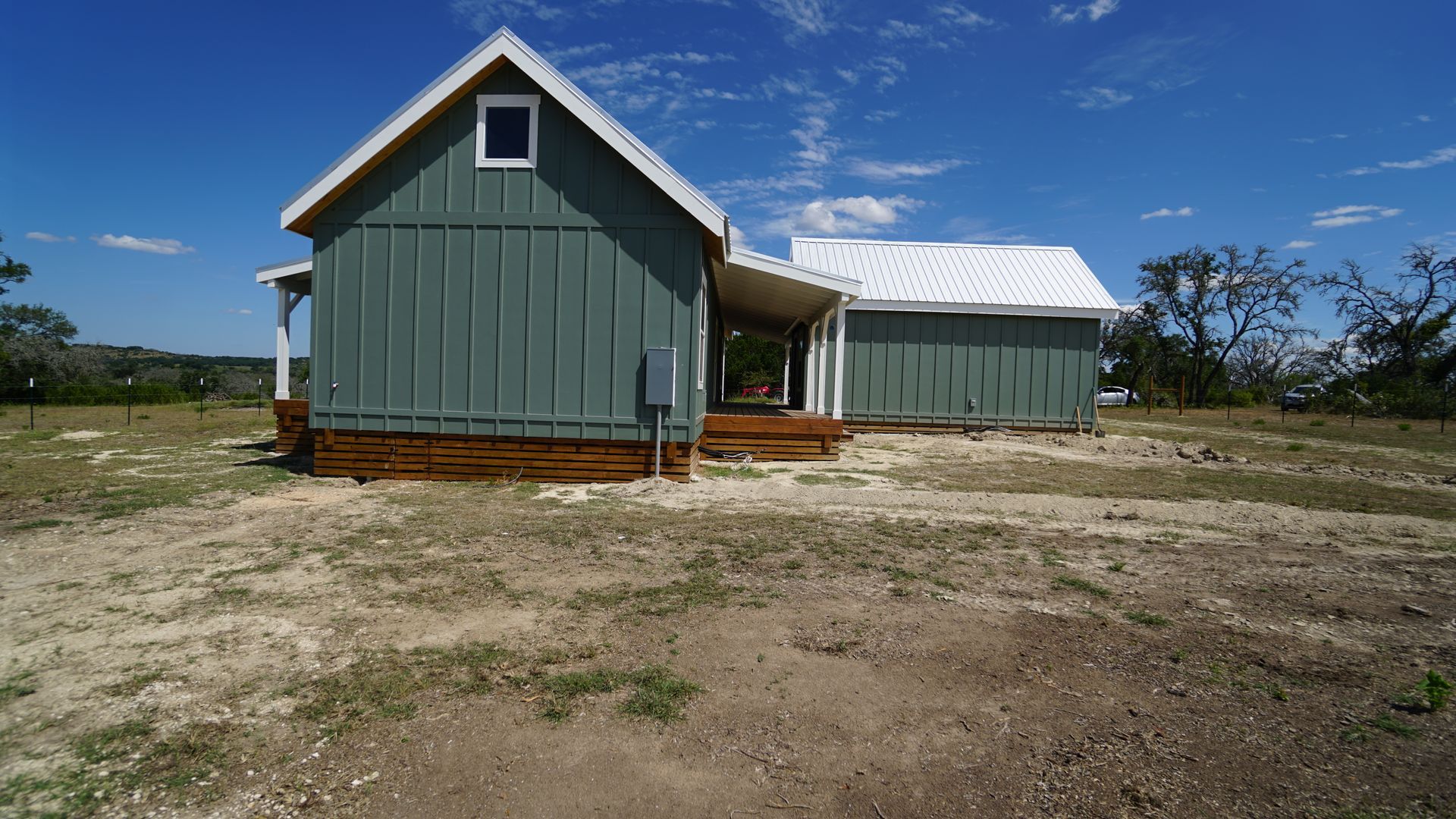 A small, teal-colored house with a white roof on a dry, grassy plot under a blue sky.