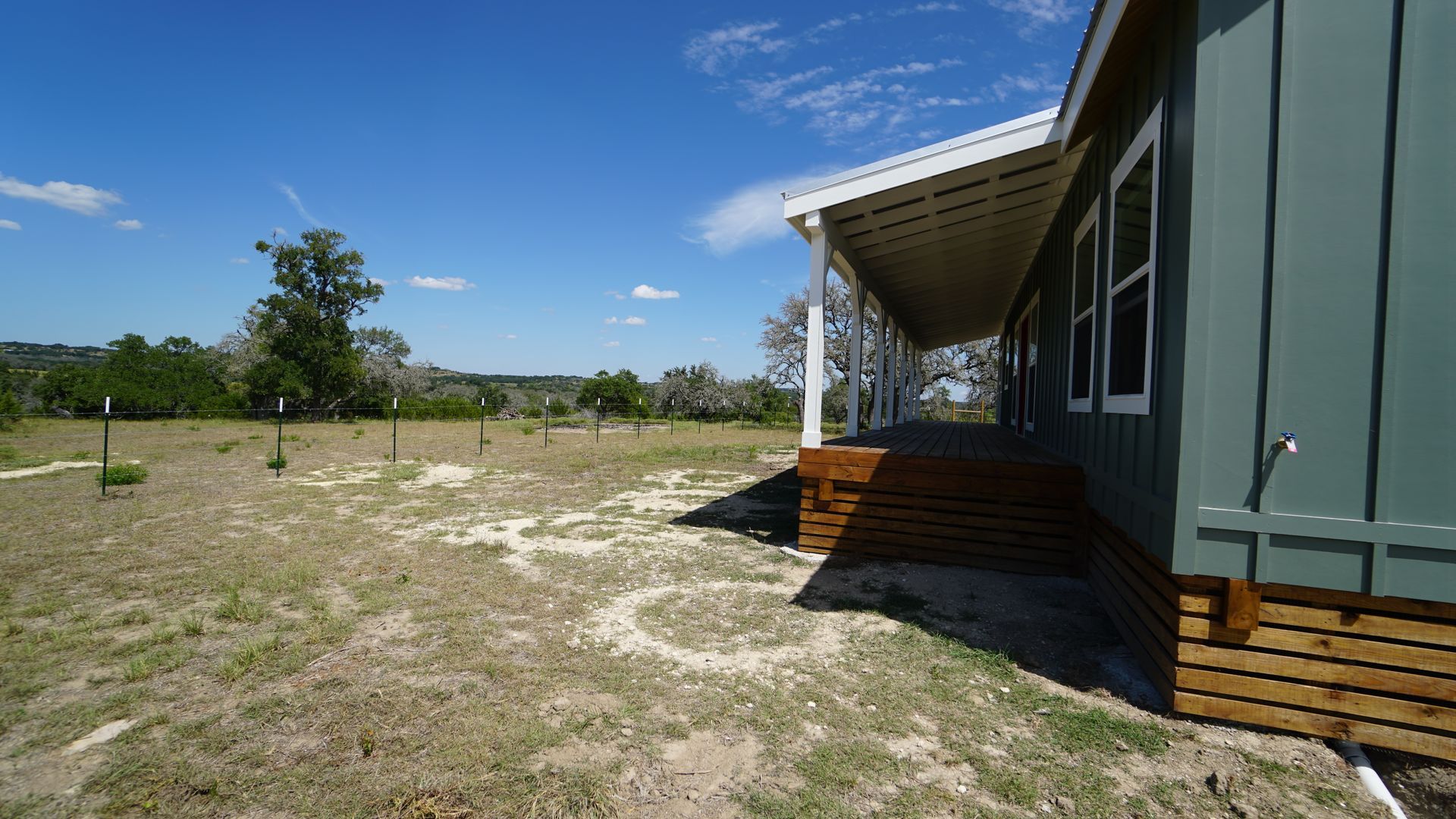 Exterior view of a teal-sided house with a porch, set in a dry grassy field under a blue sky.