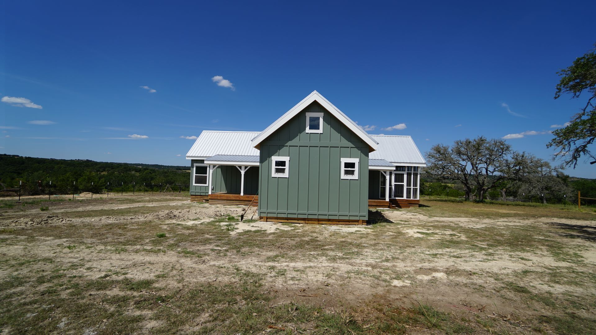 Green farmhouse with white roof against a blue sky, on a grassy plot.