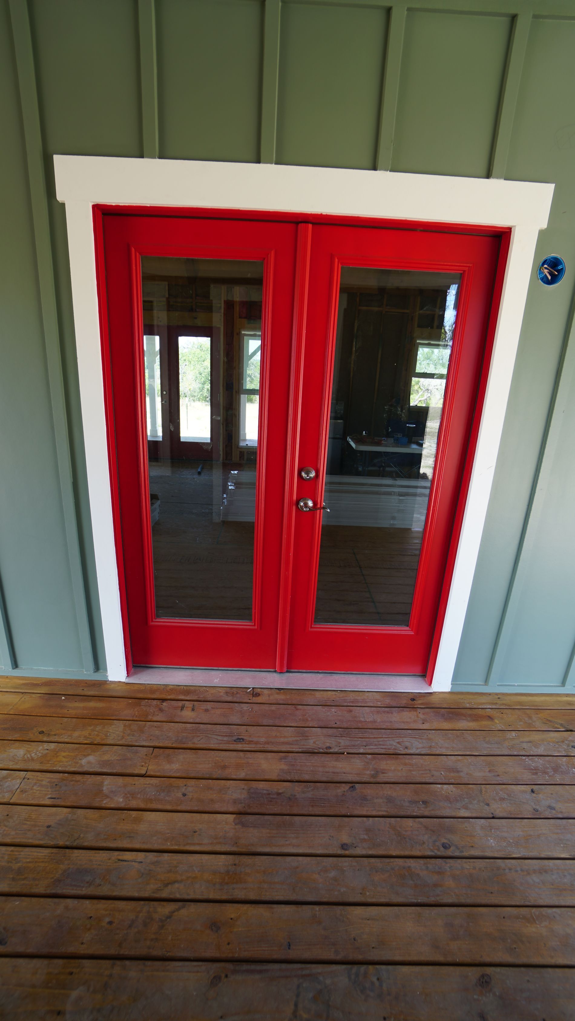 Red double doors with glass panels and white trim, on a wooden deck.