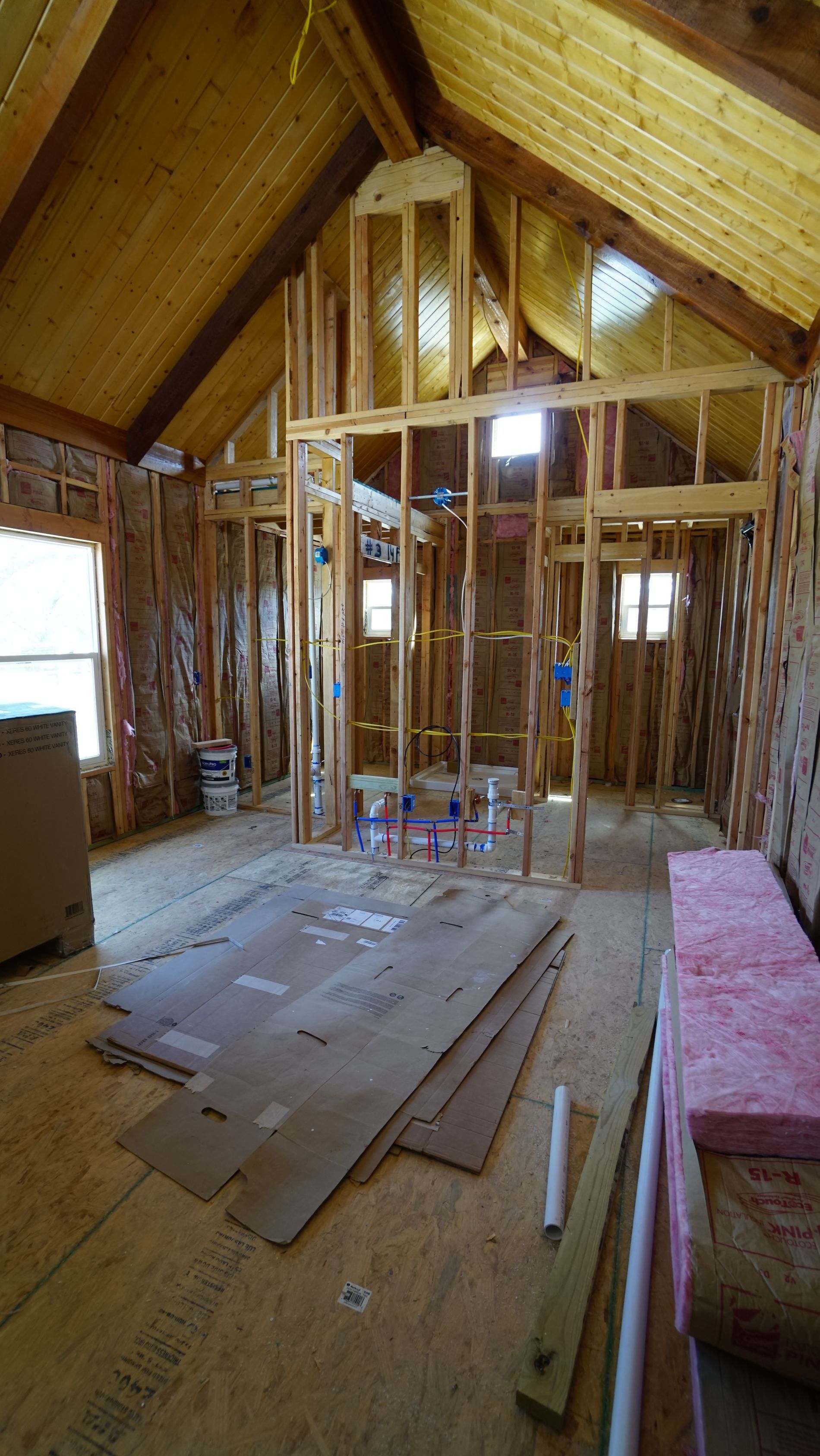 Interior of a room under construction, showing exposed wooden framing, insulation, and cardboard on the floor.