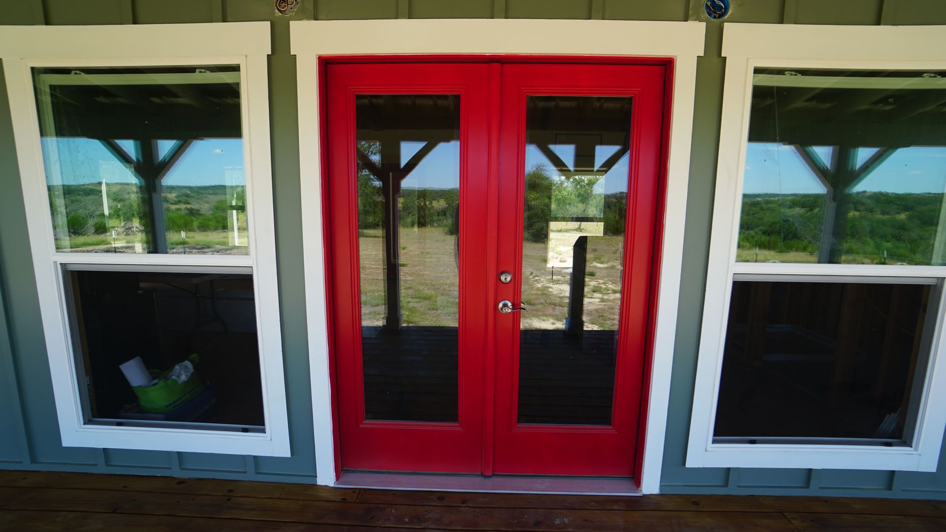 Red double doors with glass panels flanked by two windows. White trim on a green exterior.
