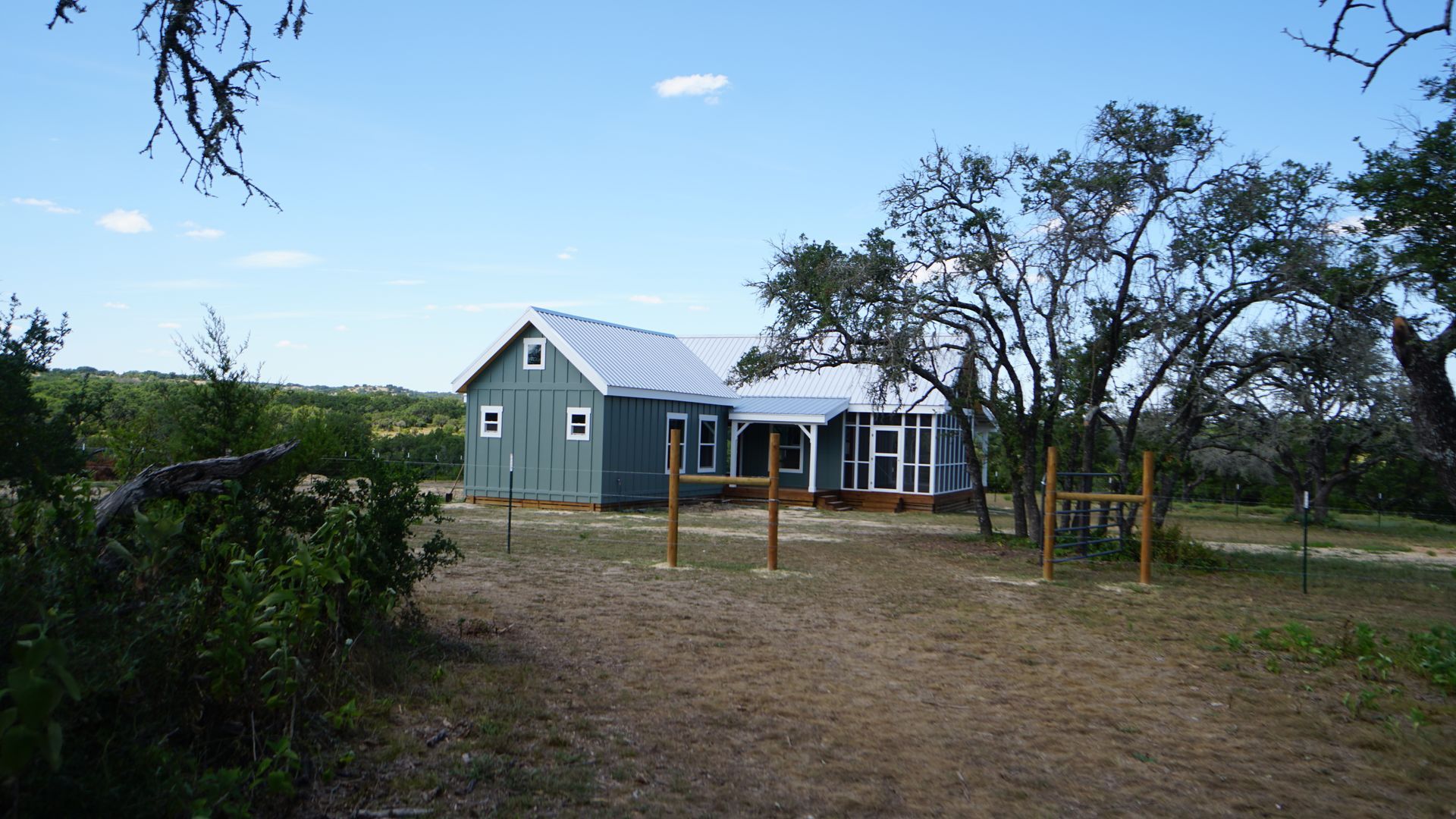 Blue-sided house with a porch and metal roof, set in a natural, grassy landscape with trees.