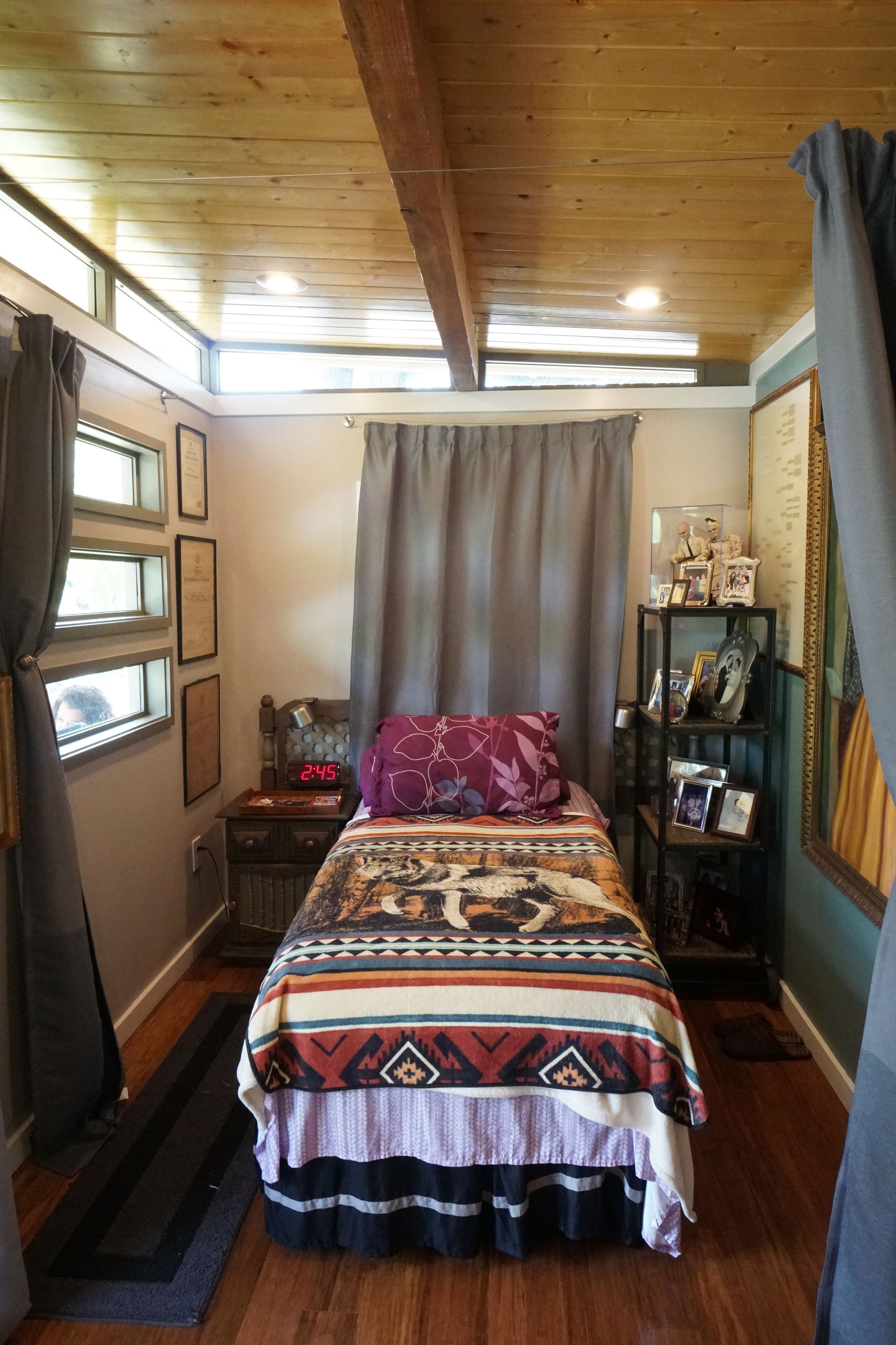 Small bedroom with a single bed, small windows, wooden ceiling, and curtains.