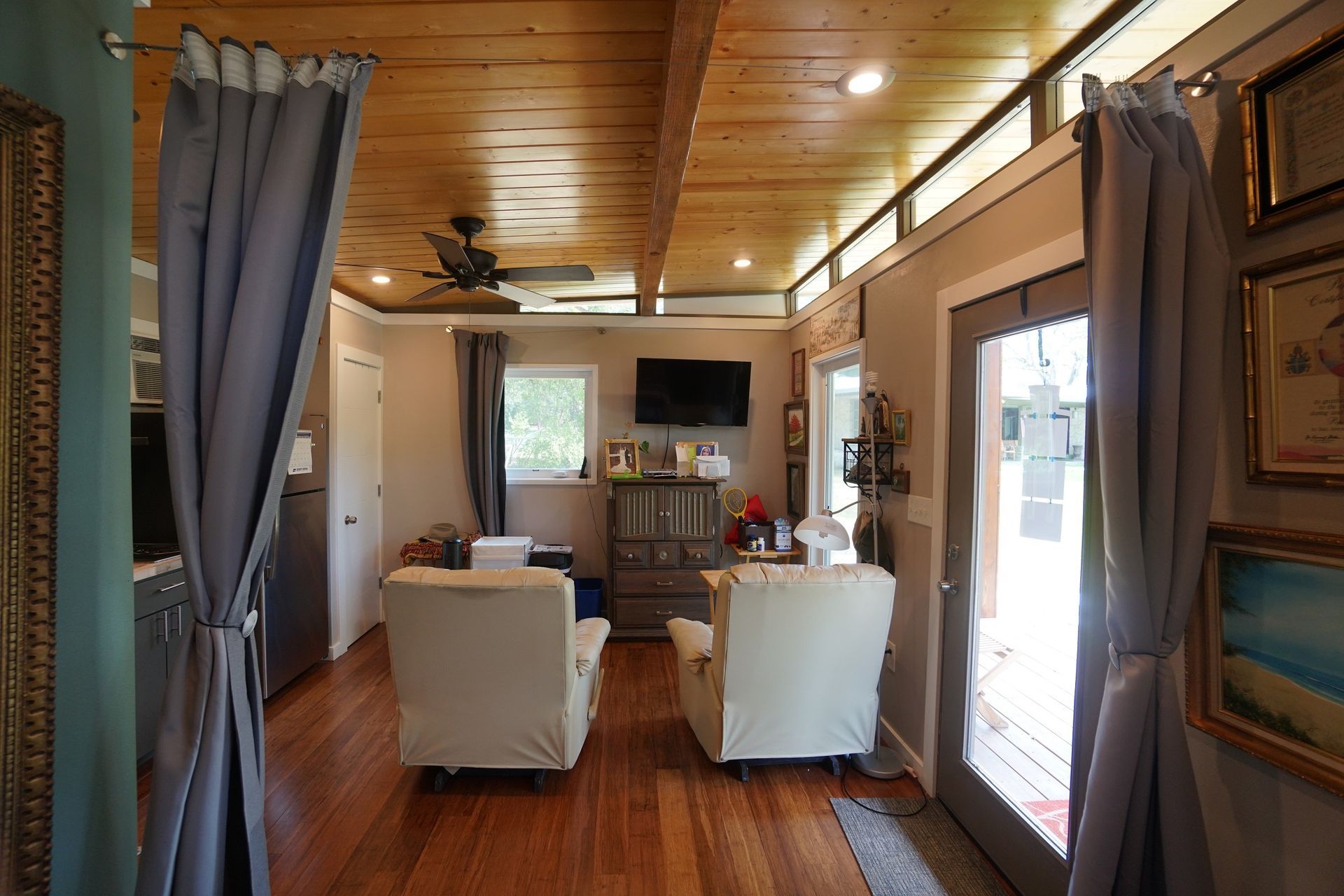 Cozy living room with wood ceiling, two cream chairs, TV, and open doorway to outdoors.