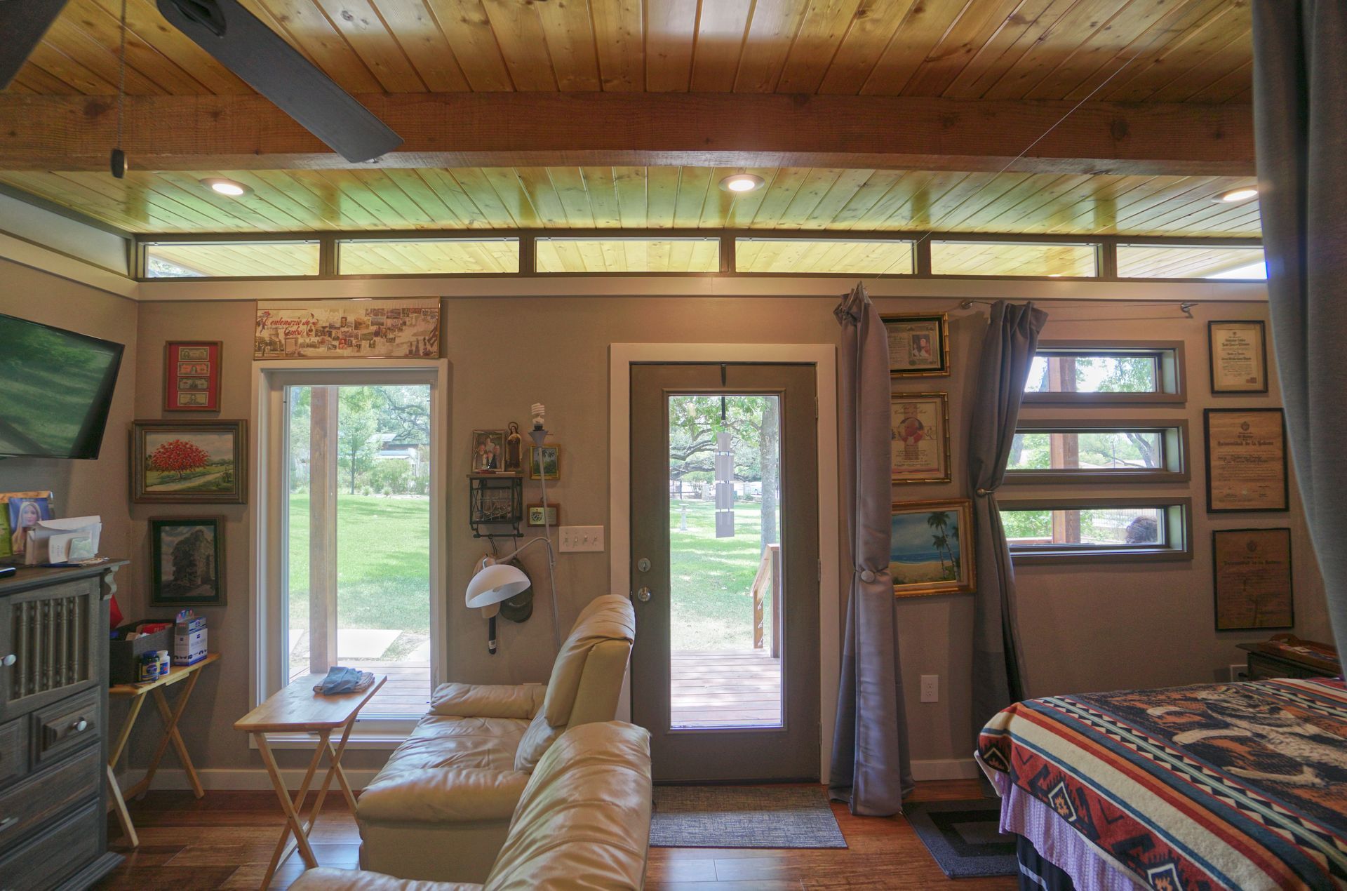 Cozy cabin interior with windows, door to outside, sofa, and bed. Wooden ceiling and neutral walls.