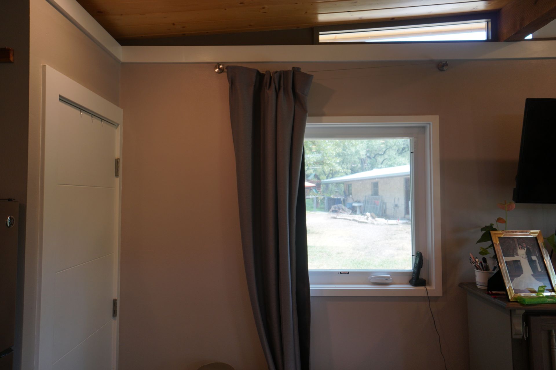 Gray curtain next to a white-framed window. A light-colored wall with a closed white door is on the left.