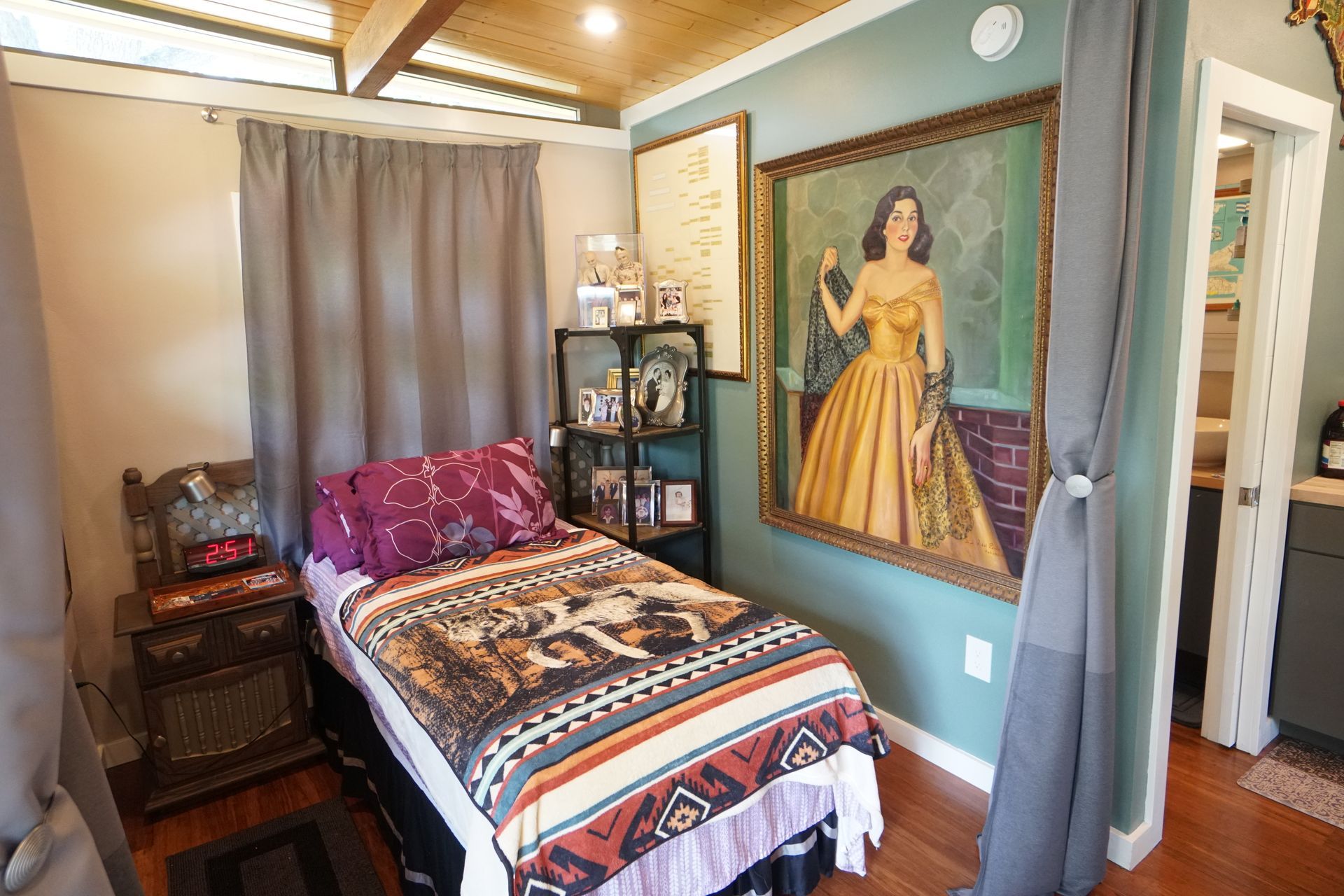 Small bedroom with a single bed, large portrait, shelves, and gray curtains.