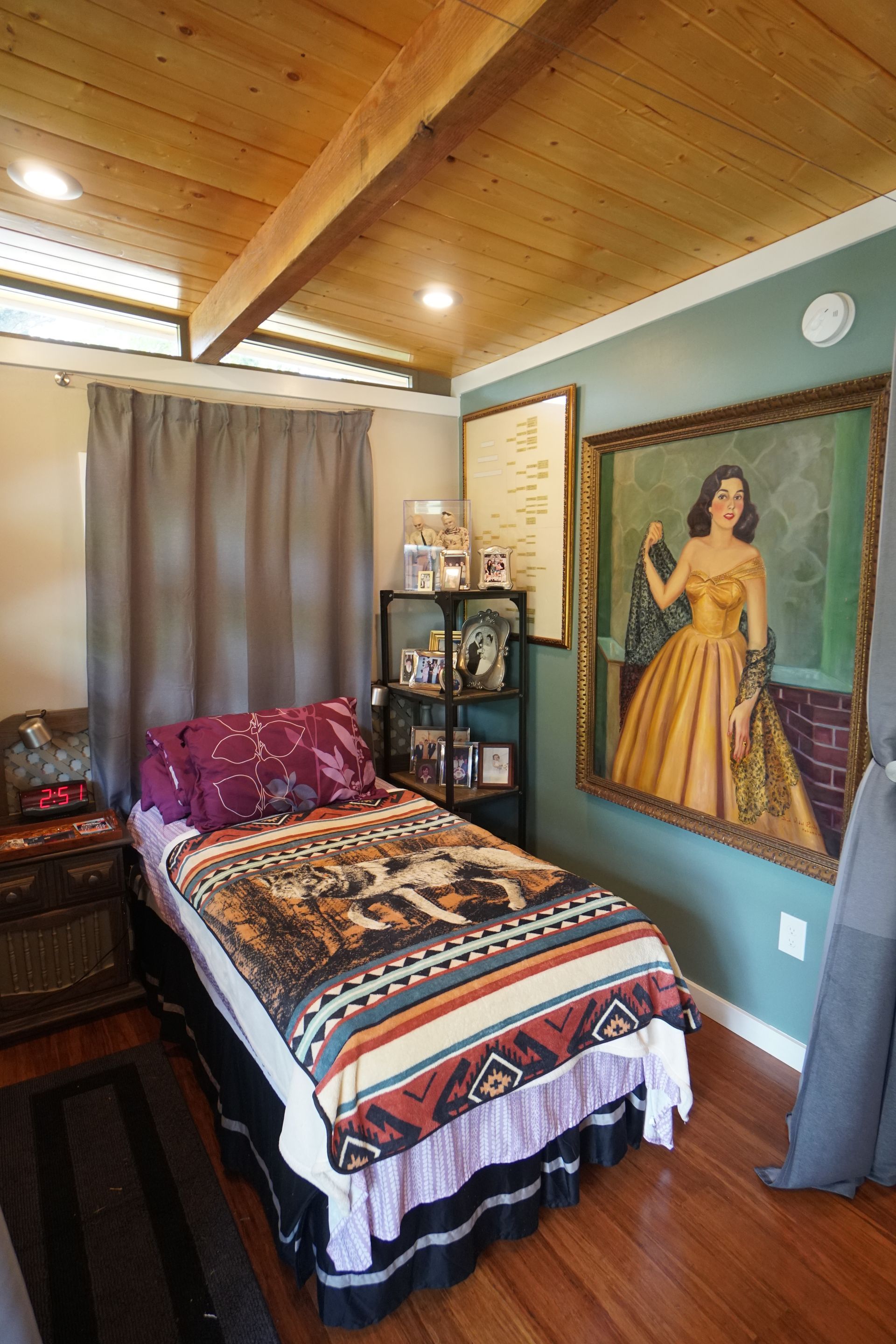 Bedroom with single bed, artwork, dark drapes, wood ceiling, and green wall.