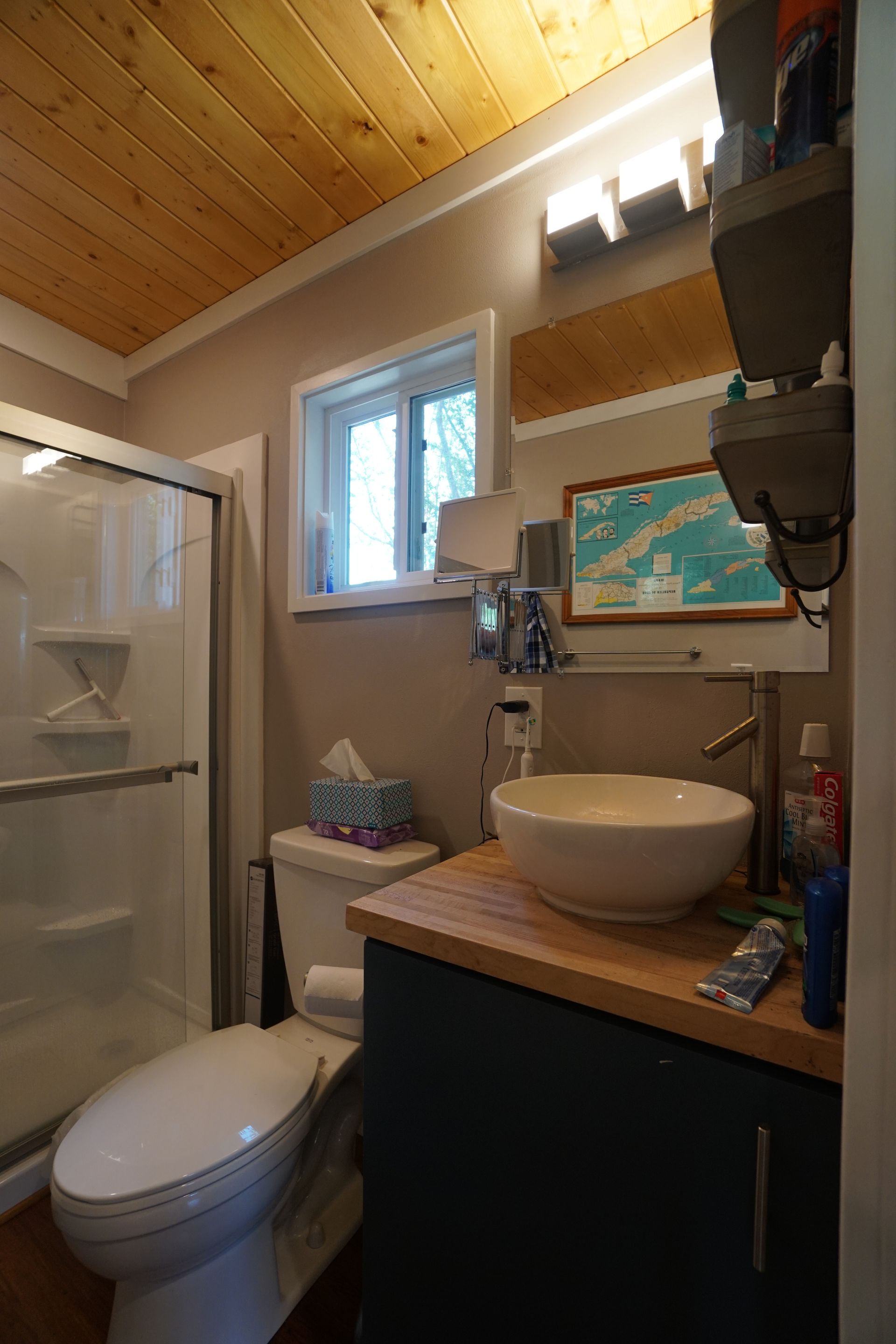 Small bathroom with a toilet, sink, and shower. Wooden ceiling, beige walls, and a window.