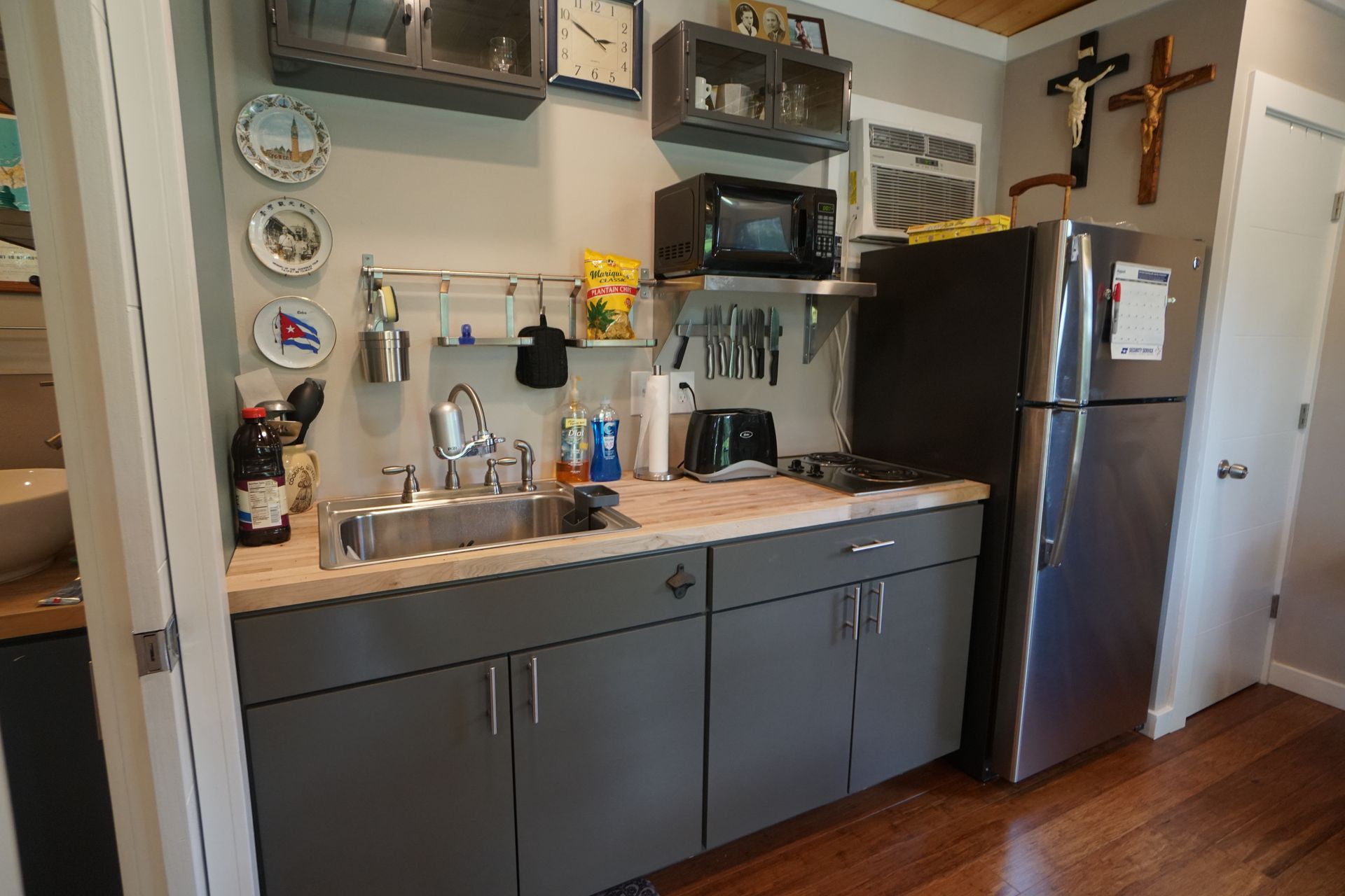 Small kitchen with gray cabinets, stainless steel fridge, microwave, and sink, wooden countertop.