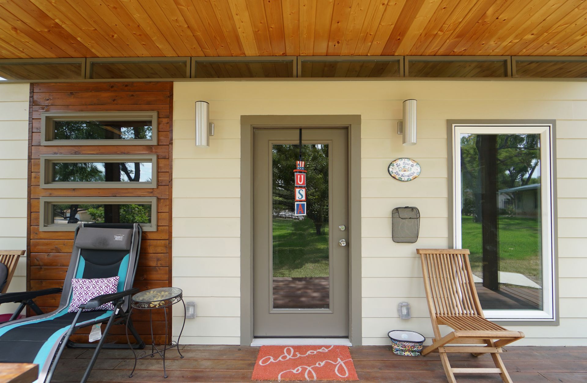 Exterior of a house with a wooden porch ceiling, a door, and windows; two chairs are on the porch.